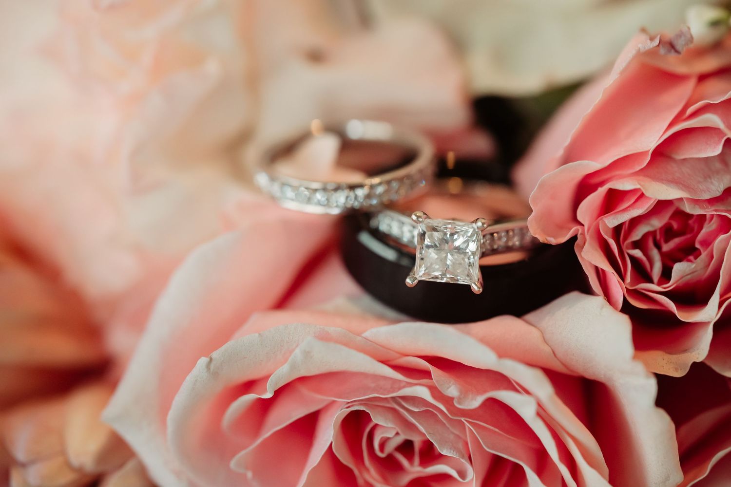 Diamond engagement ring nestled among soft pink roses and flowers.