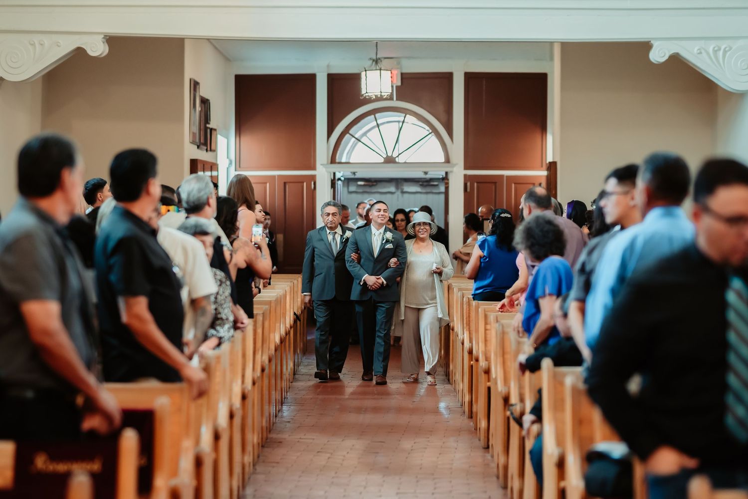 Wedding guests line up in wooden pews of a traditional church sanctuary during a ceremony.