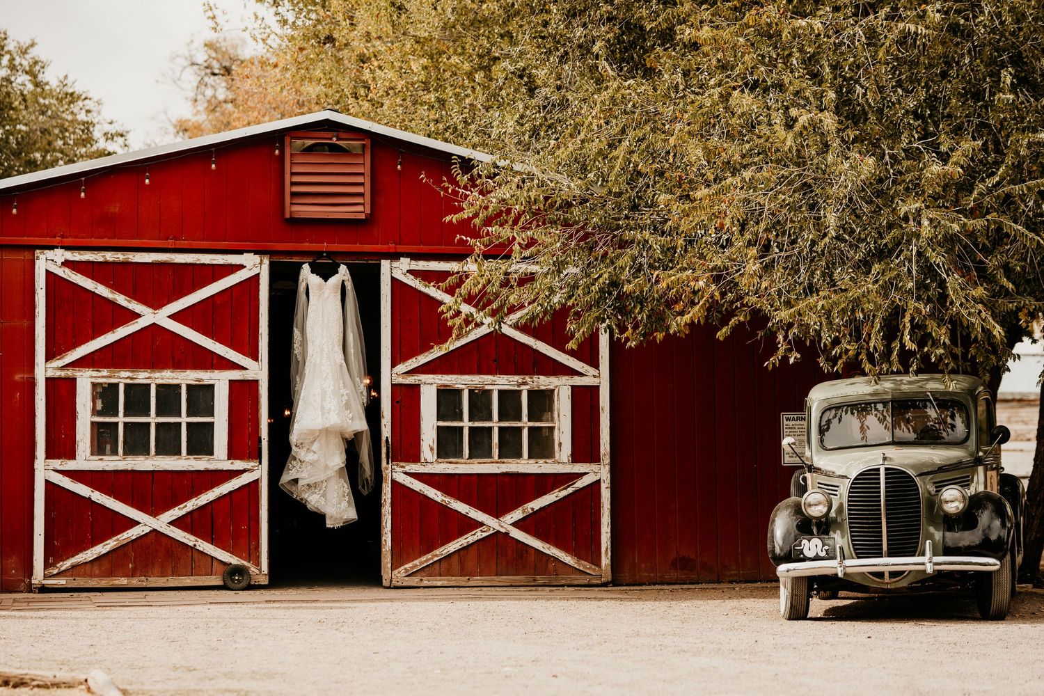 Classic red and white barn buildings with rustic barn doors and windows stand in a row against autumn trees.