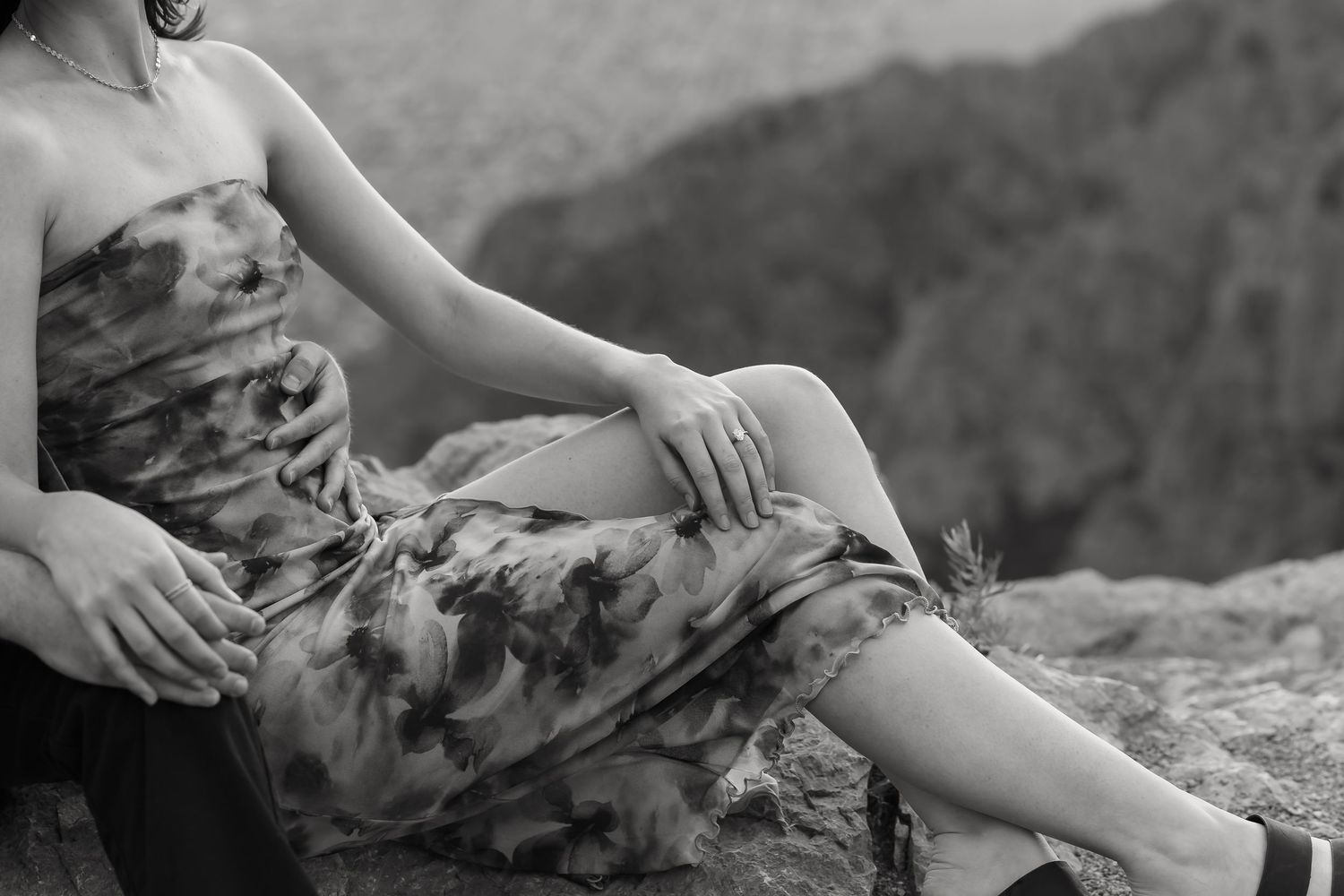 Black and white image of two people sitting close together on rocky mountain terrain.
