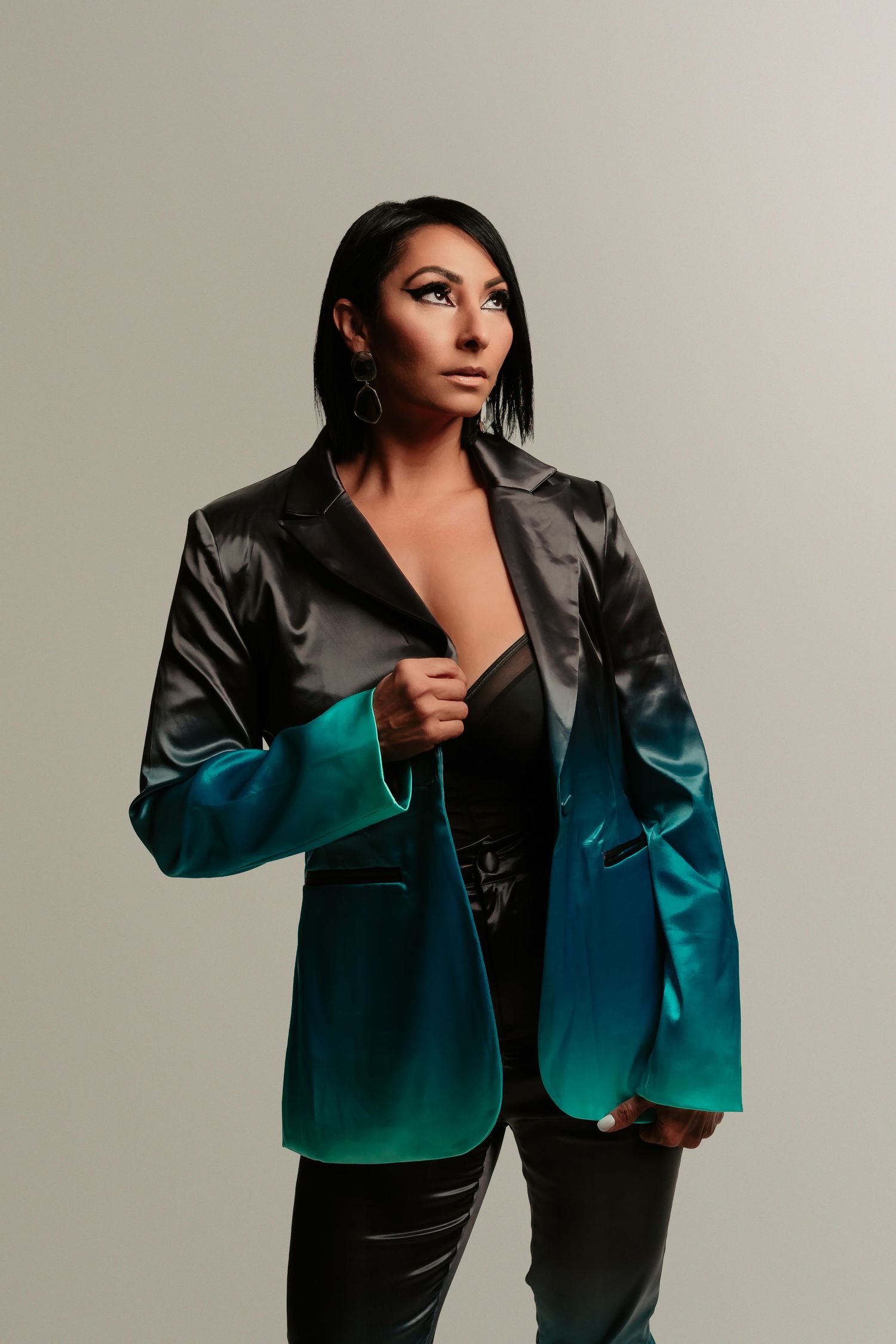 Fashion model wearing gradient black to teal ombre blazer jacket in dramatic studio lighting poses against neutral background.