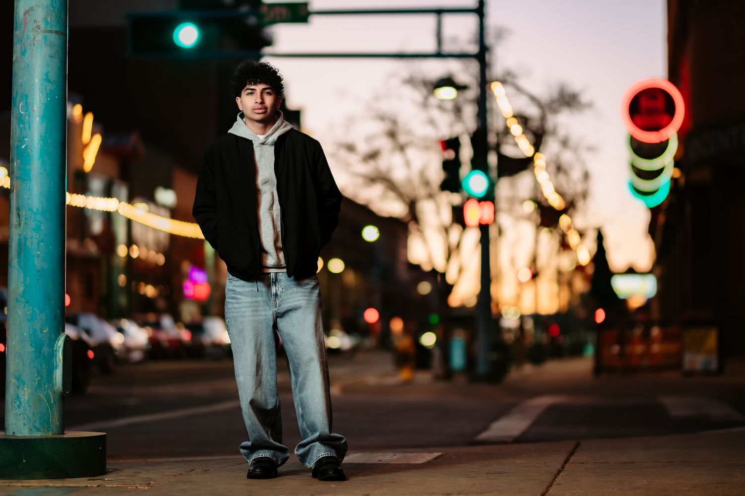 Person walking on urban street at night with colorful bokeh lights and illuminated storefronts in background.