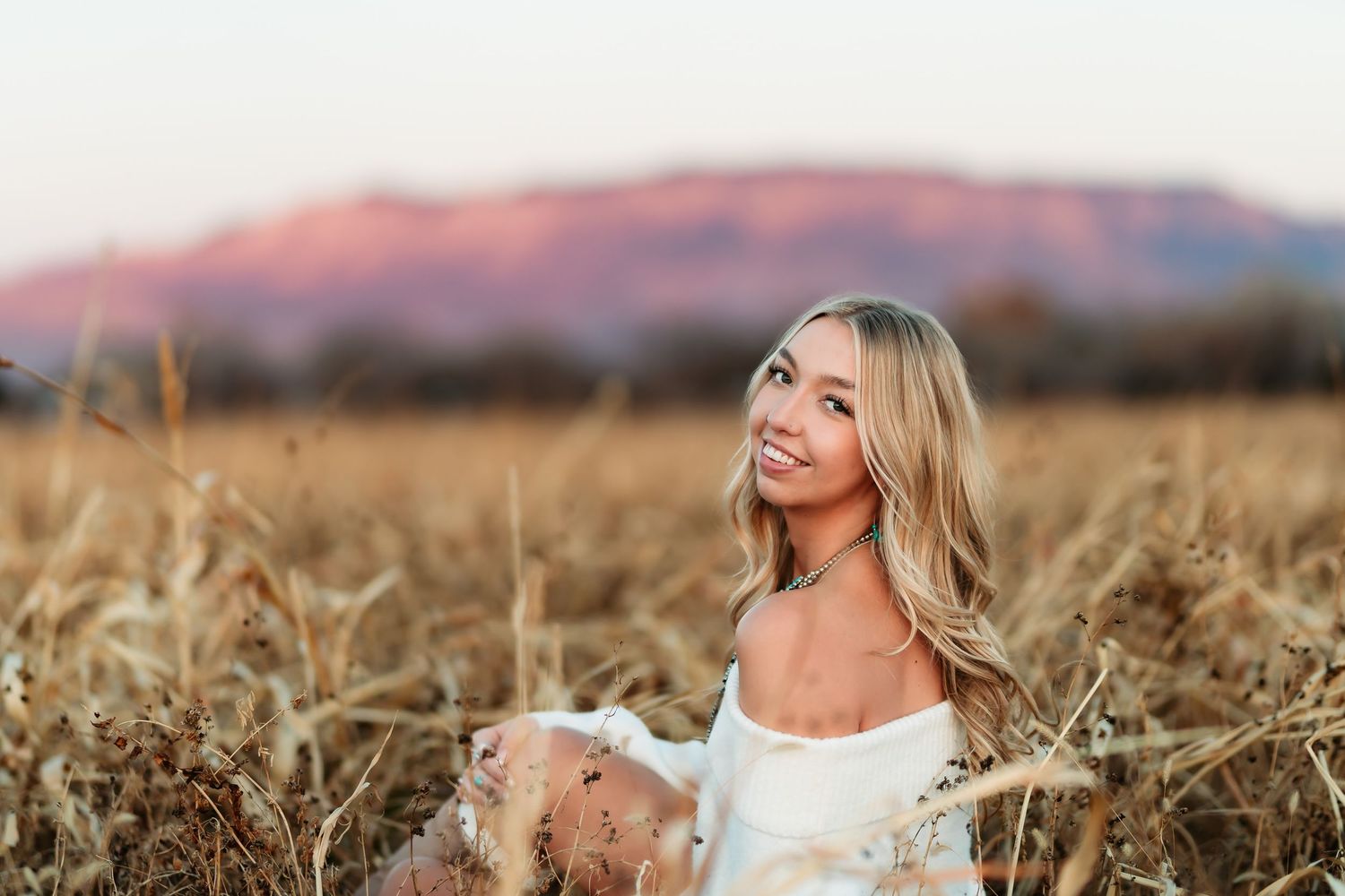 A woman in a white dress laughs joyfully while standing in a golden wheat field at sunset.