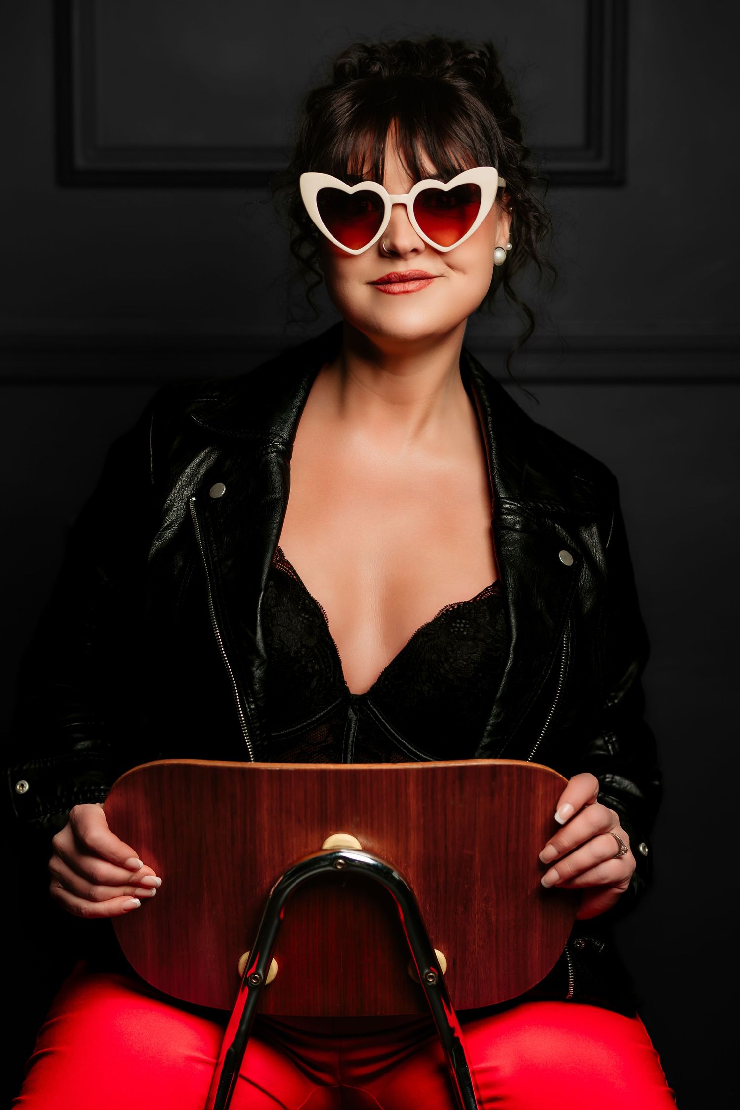 Stylish heart-shaped sunglasses and black jacket against dark background with red accent lighting.