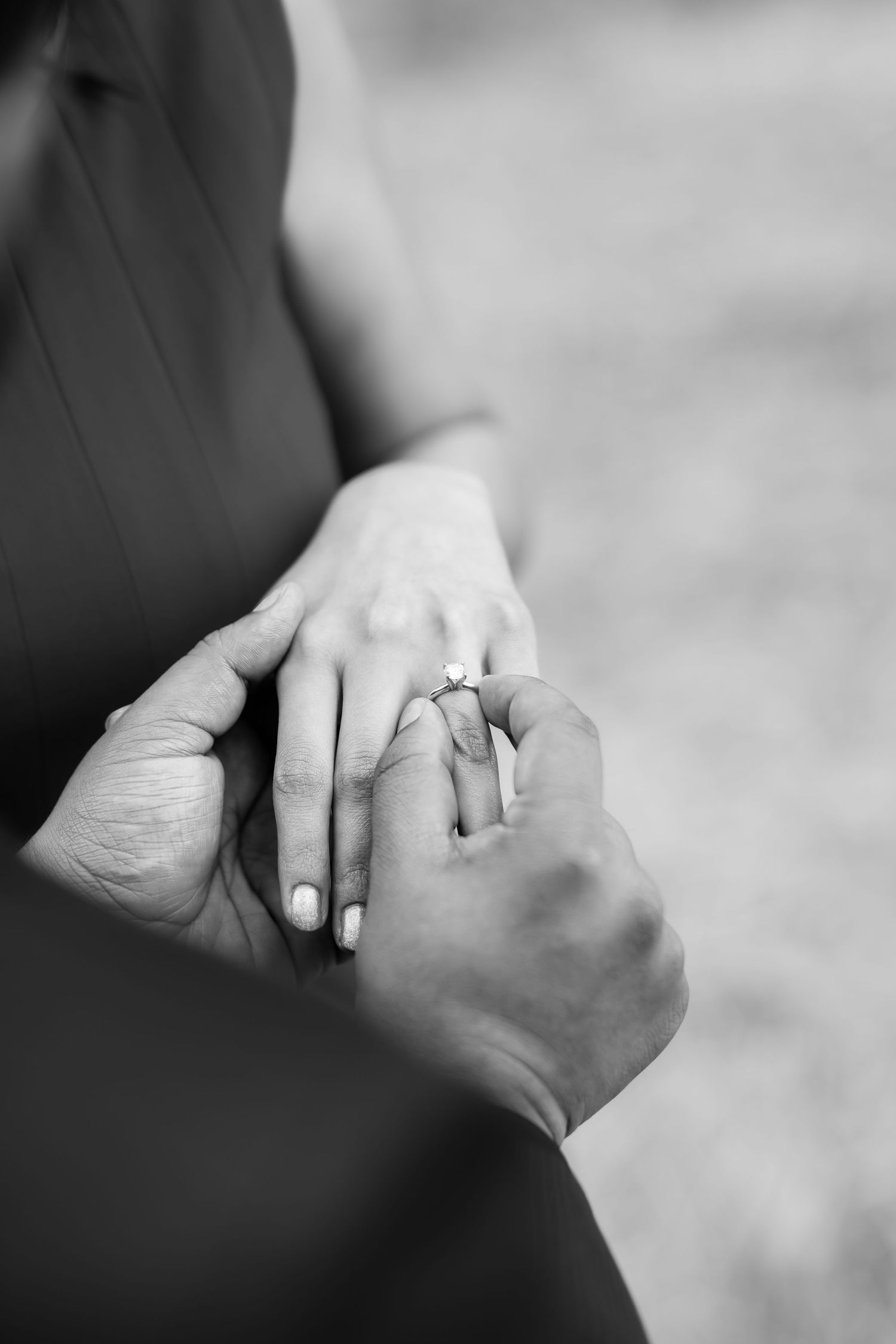 Close-up black and white shot of hands exchanging an engagement ring.