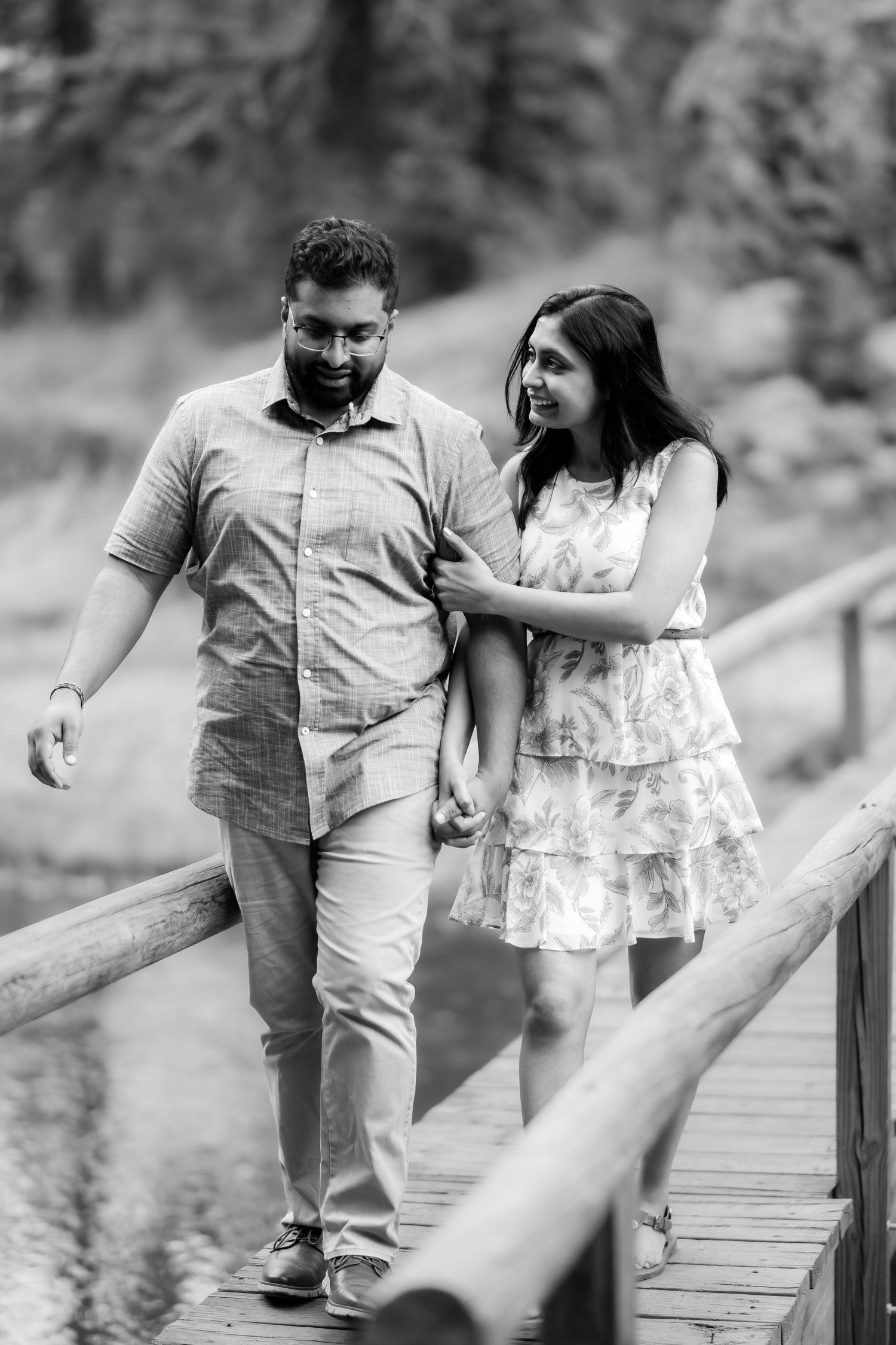 A couple walks intimately together along a wooden boardwalk surrounded by nature in black and white.