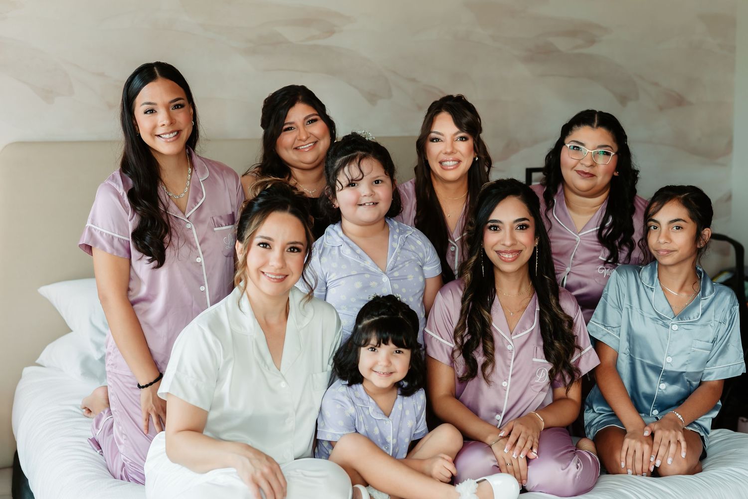 Family members in matching soft blue and pink loungewear smile together on floor in studio setting.