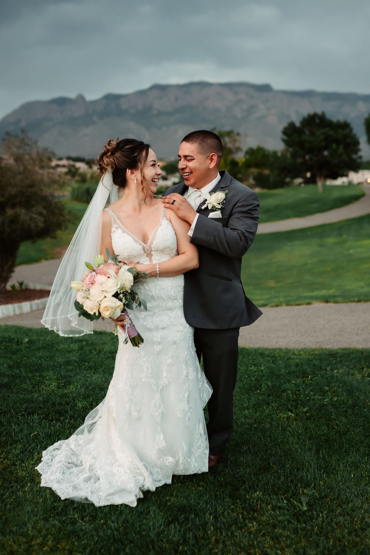 Wedding couple shares a romantic moment on a golf course with mountains and dramatic clouds in the background.