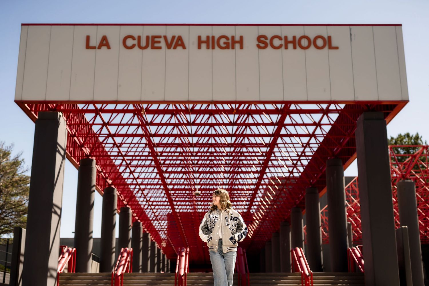 Student in white outfit stands beneath red geometric canopy at La Cueva High School entrance.