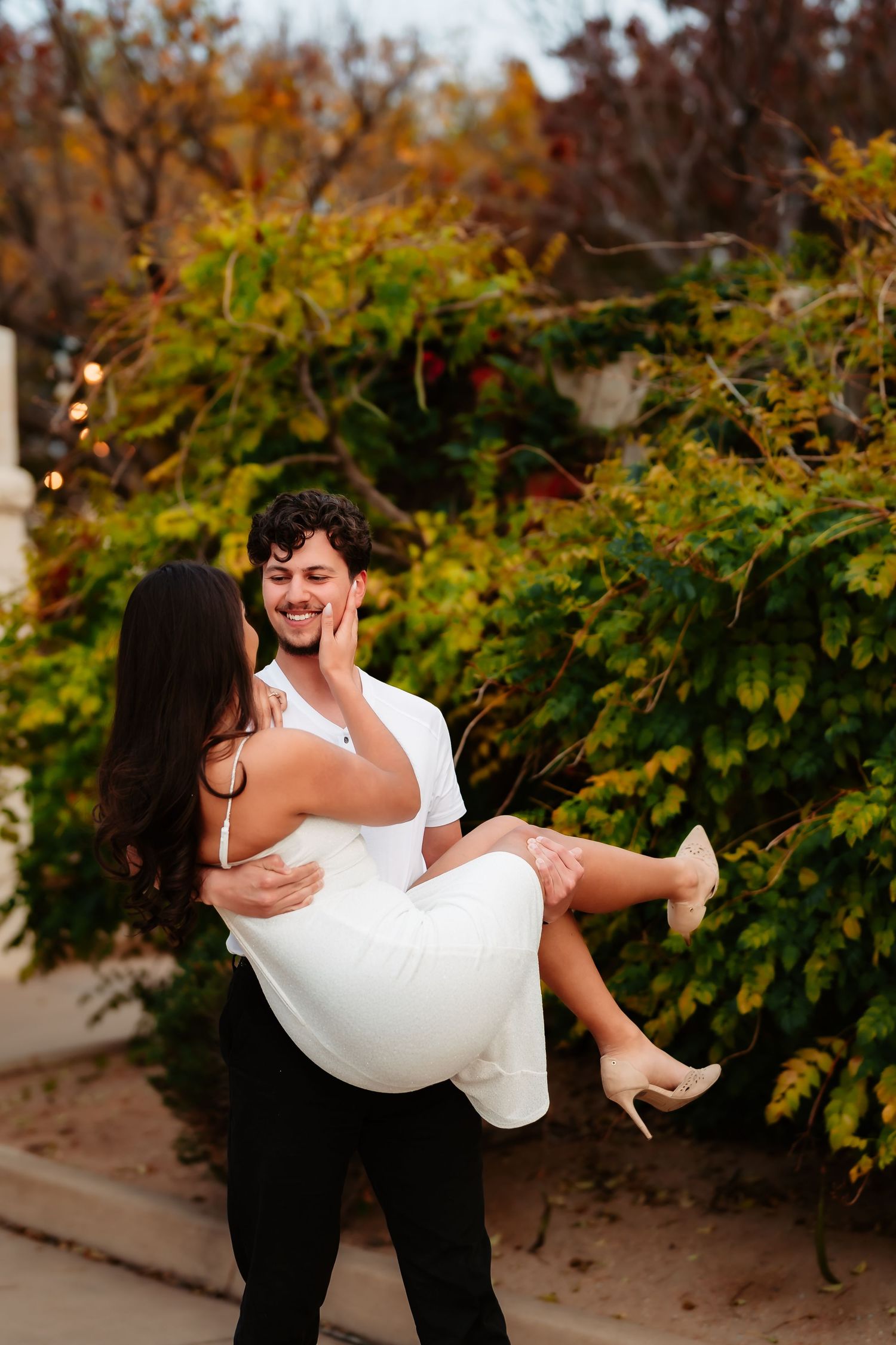 A romantic couple shares a playful moment in front of autumn foliage as one lifts the other in a series of photos.