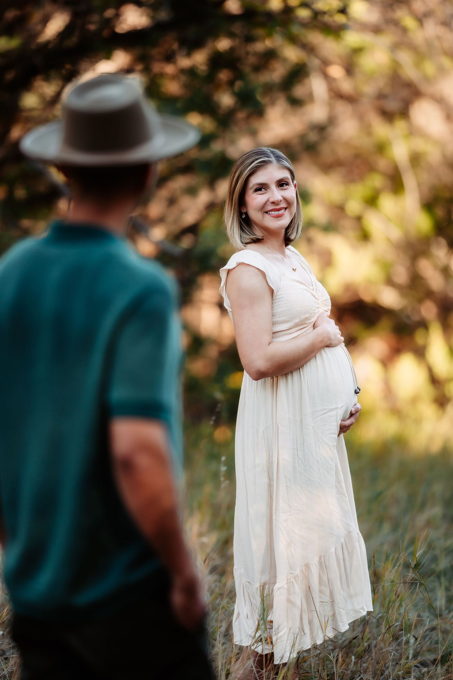 A romantic outdoor maternity photo session with a couple in a sunlit natural setting.