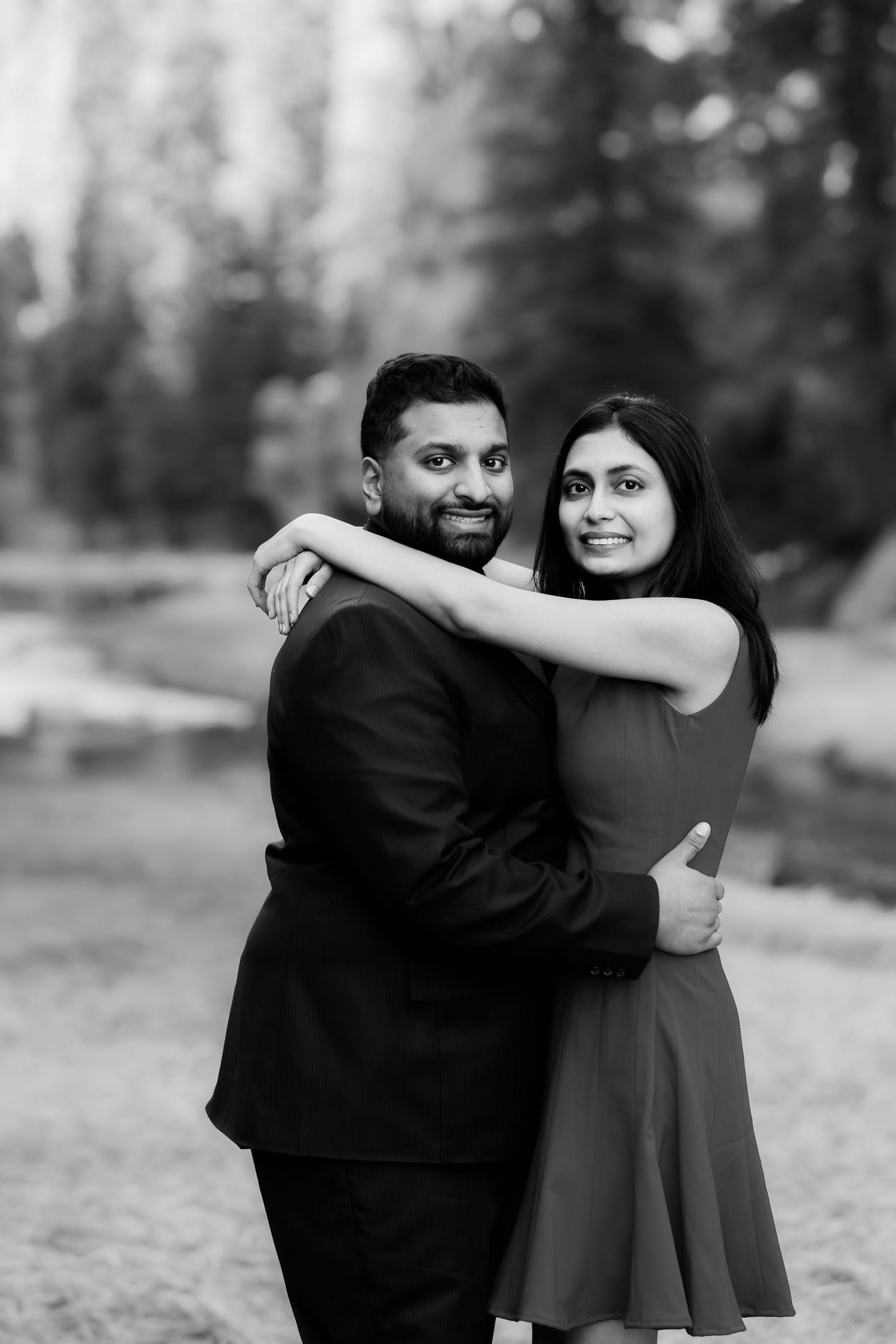 A black and white portrait of a couple embracing outdoors in formal attire.