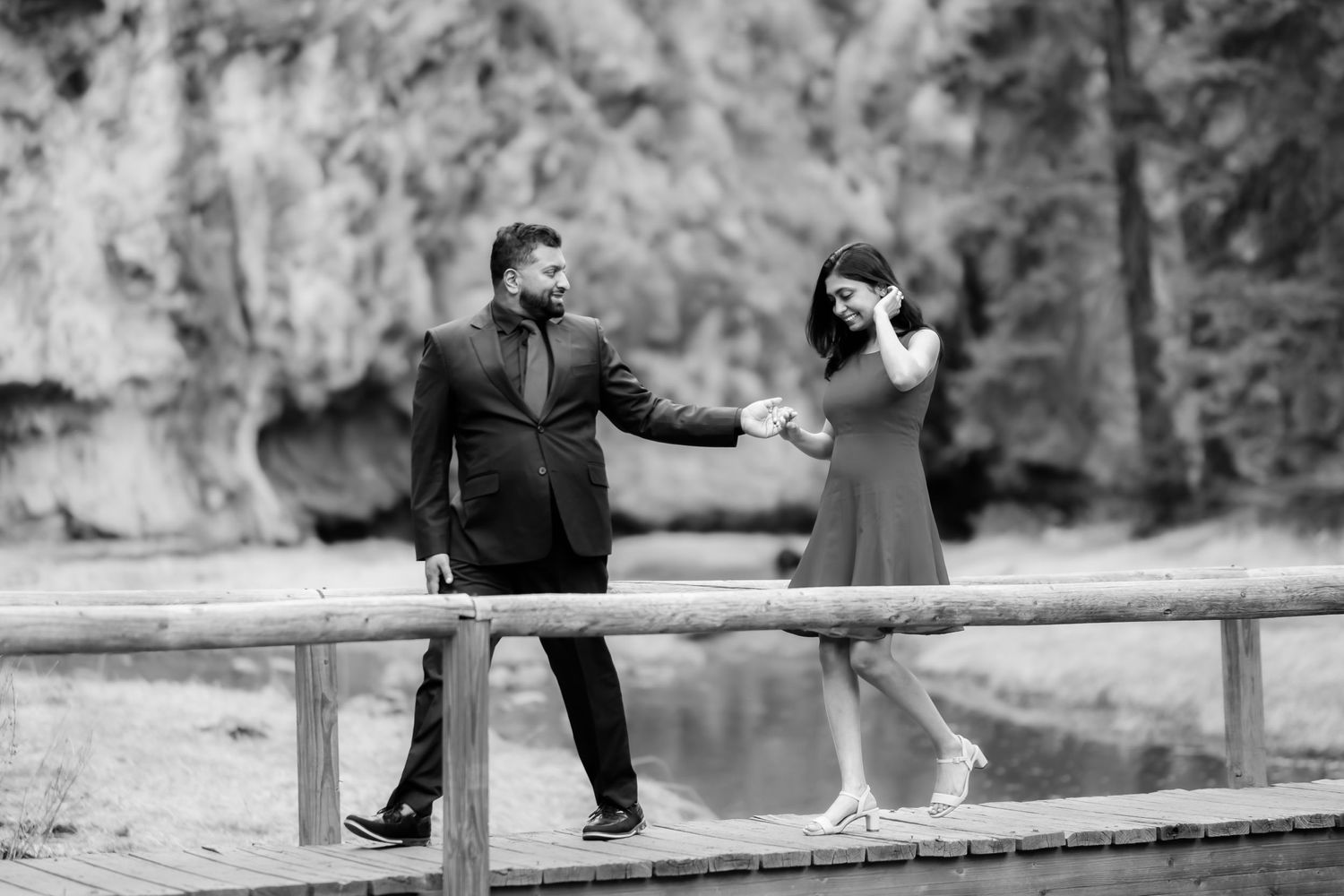 Playful couple dancing on wooden bridge in scenic mountain landscape.