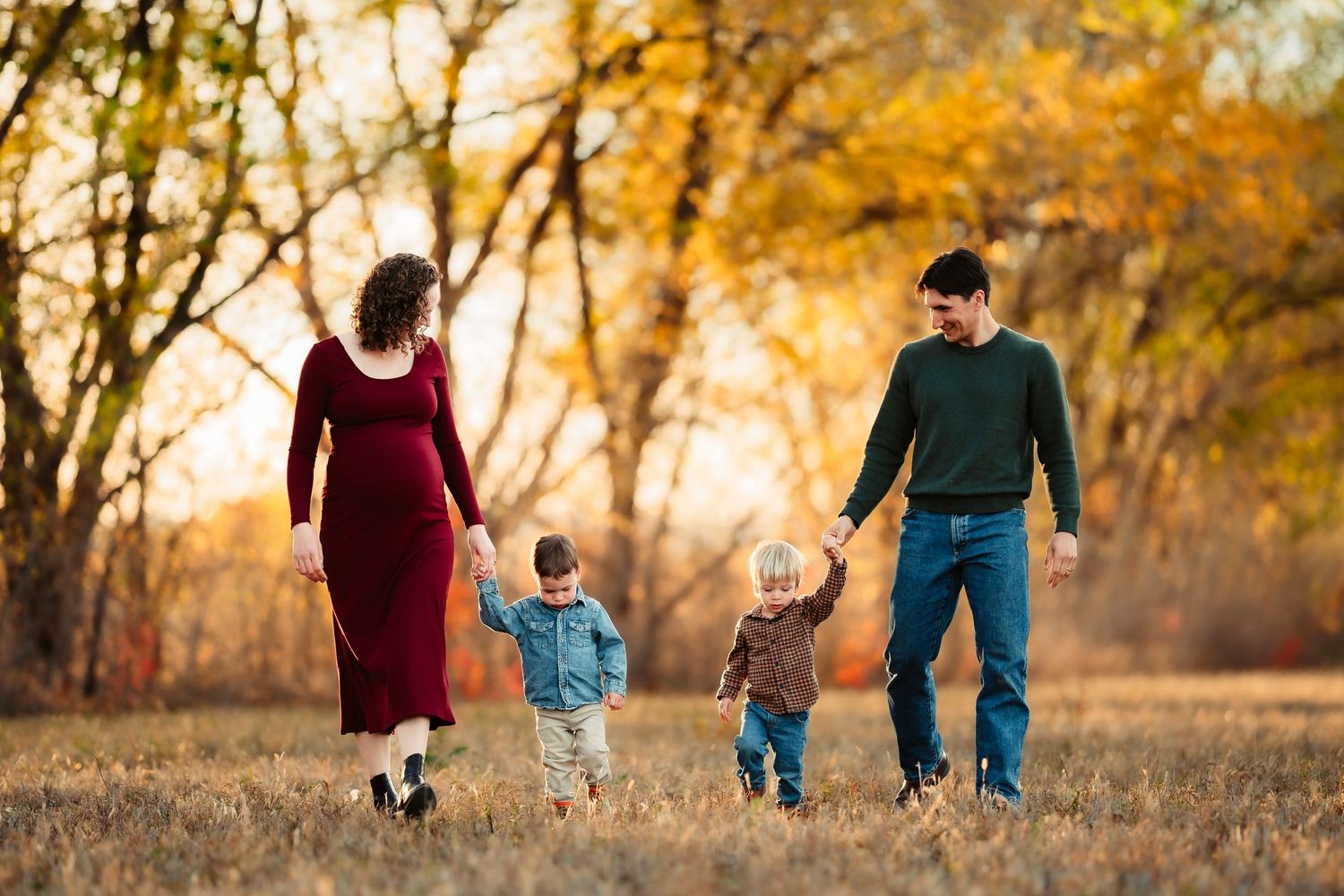 Family walking together through a golden autumn field at sunset casting long shadows on the grass.