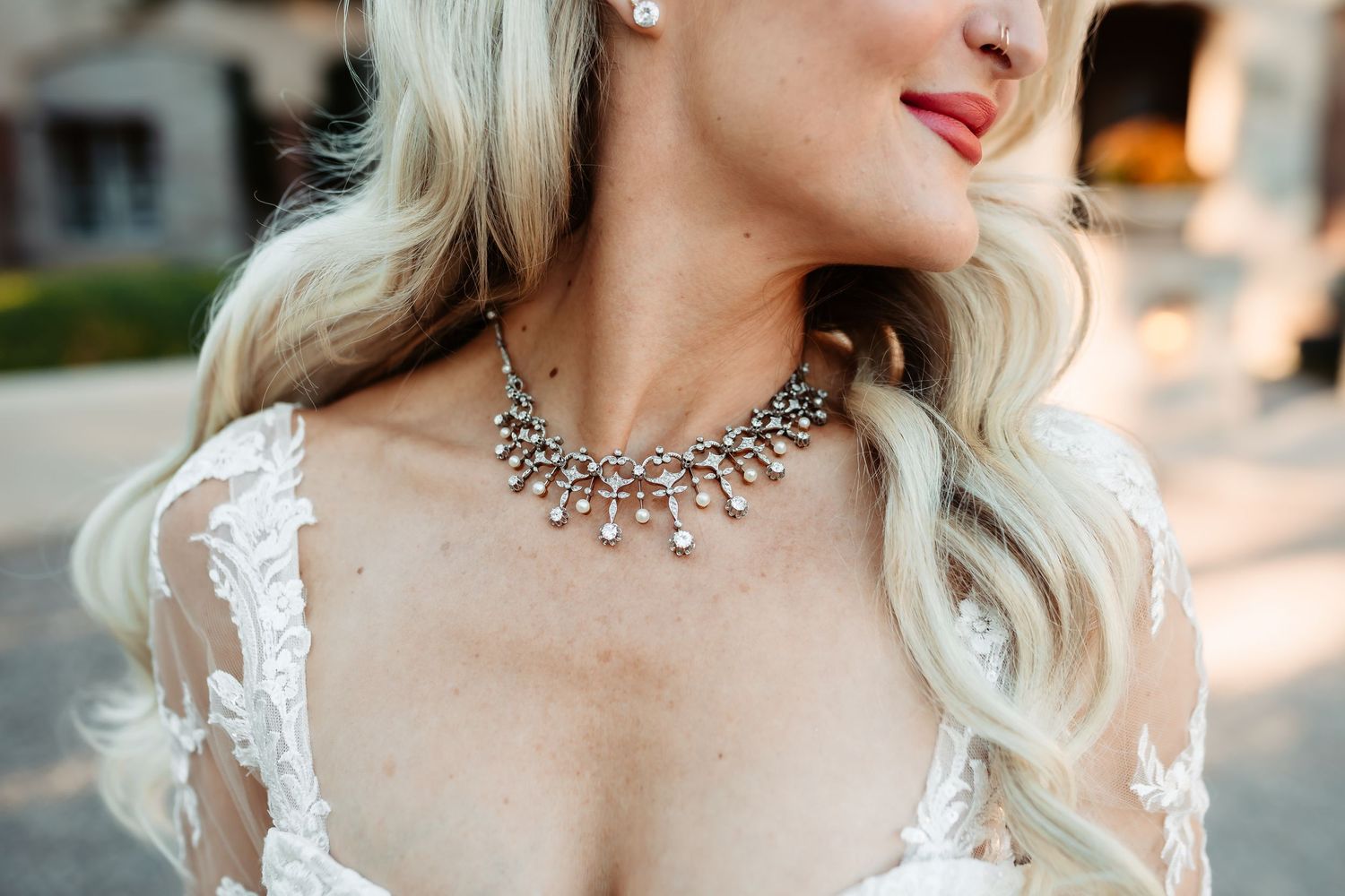 Close up detail of silver crystal statement necklace and white lace dress with platinum blonde wavy hair.