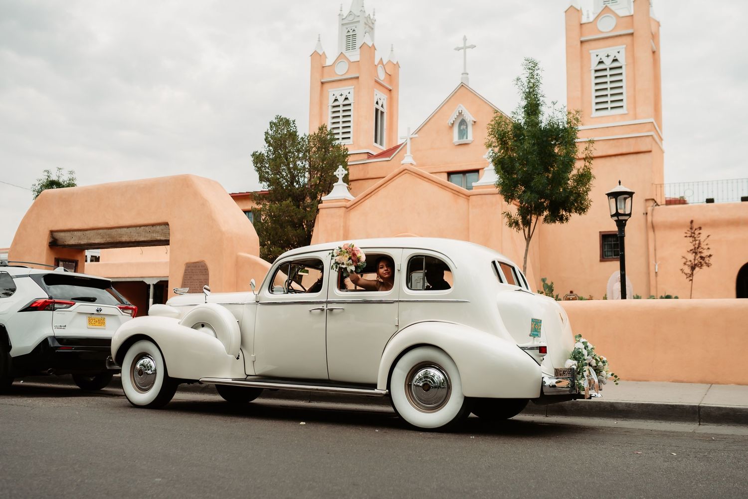 Vintage white car parked in front of historic San Felipe de Neri Church with its distinctive pink adobe facade in Albuquerque.