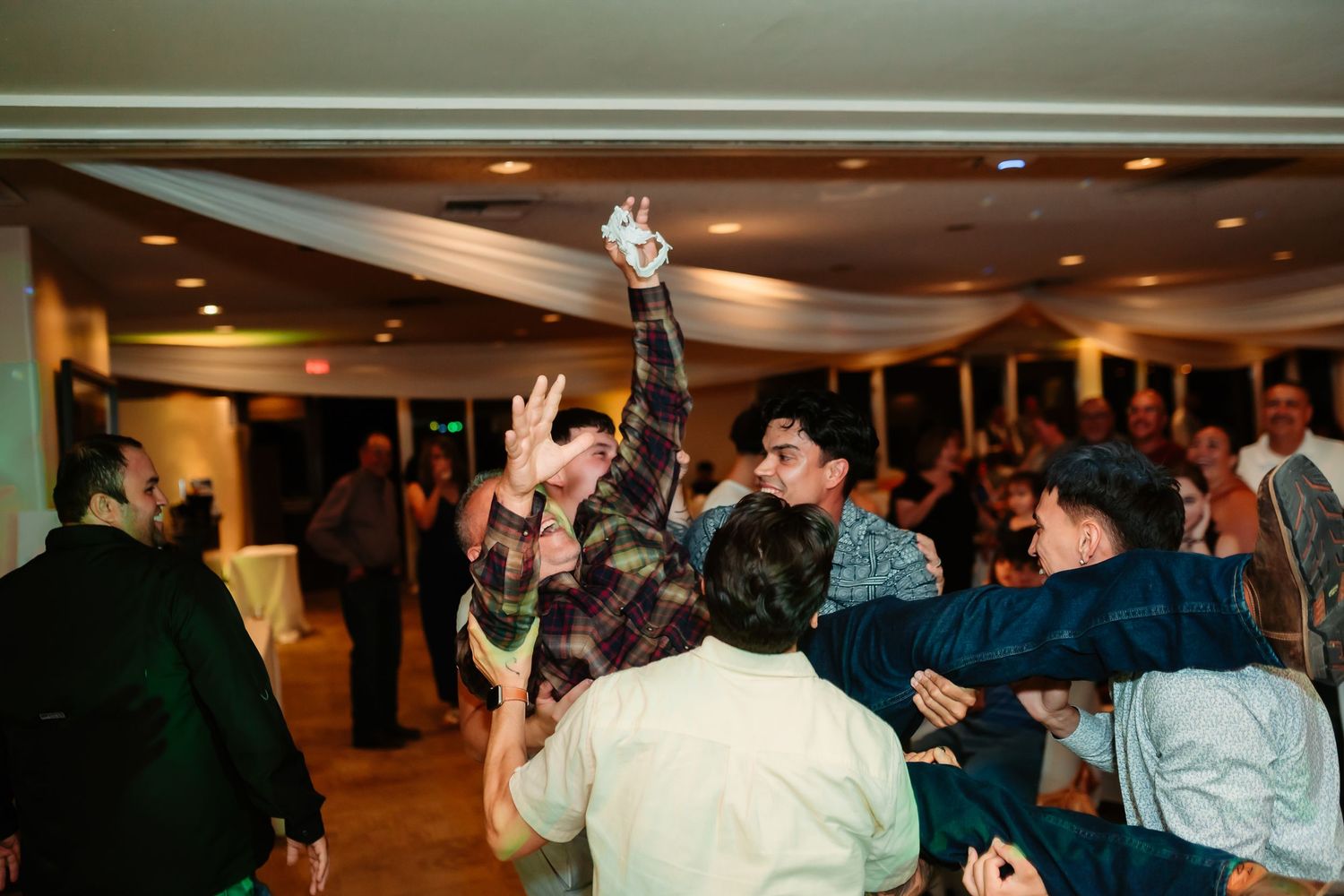 A large group dances and socializes at an indoor party with ambient lighting.