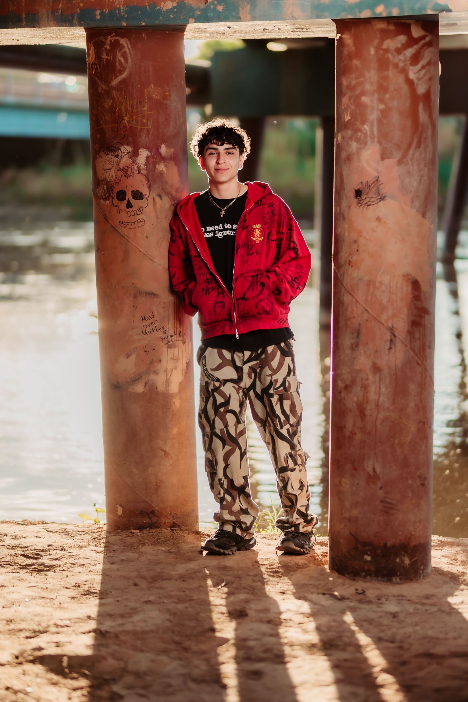 Urban fashion photo between concrete columns with skull graffiti and dramatic lighting.