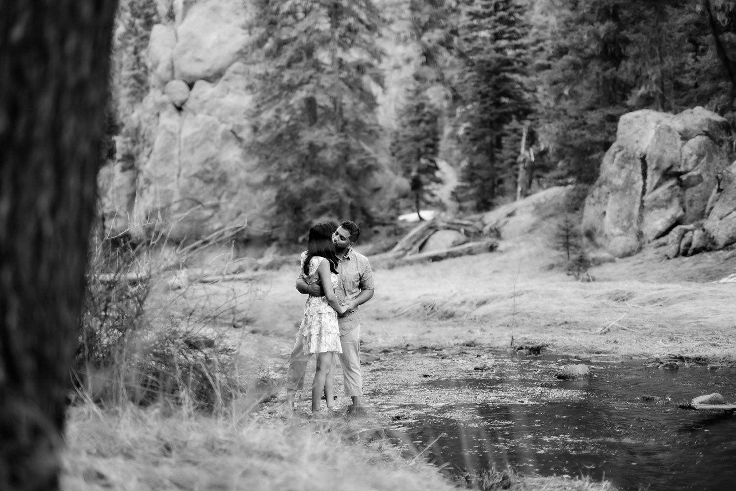 A couple embracing in a scenic mountain landscape with a stream in the background.
