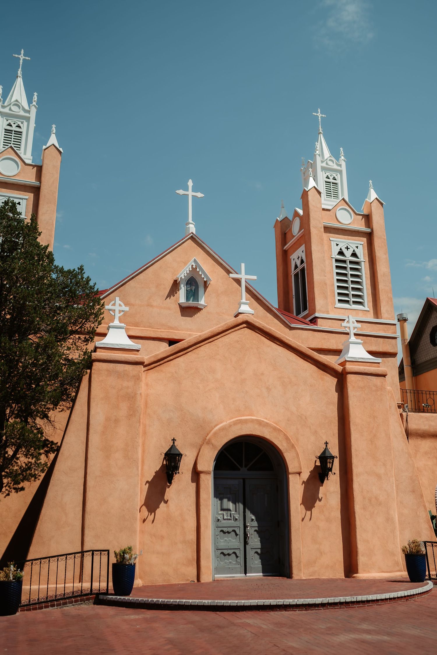 Historic adobe church exterior with white crosses and bell towers against blue sky in New Mexico.