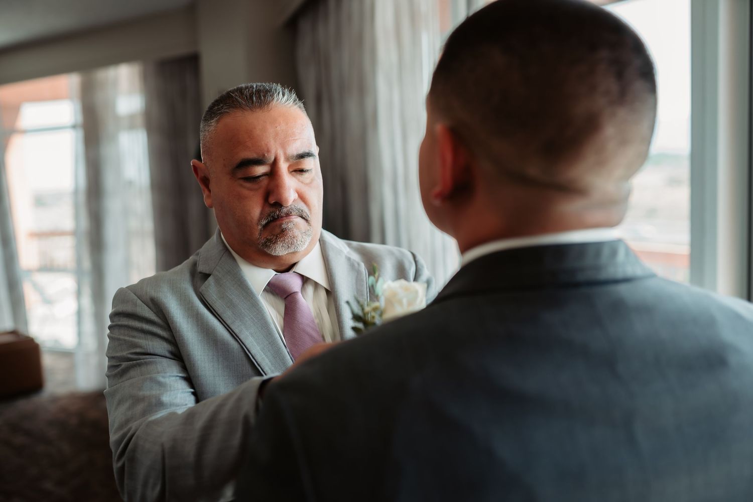 Formal wedding preparation scene in modern room with large windows and urban backdrop.