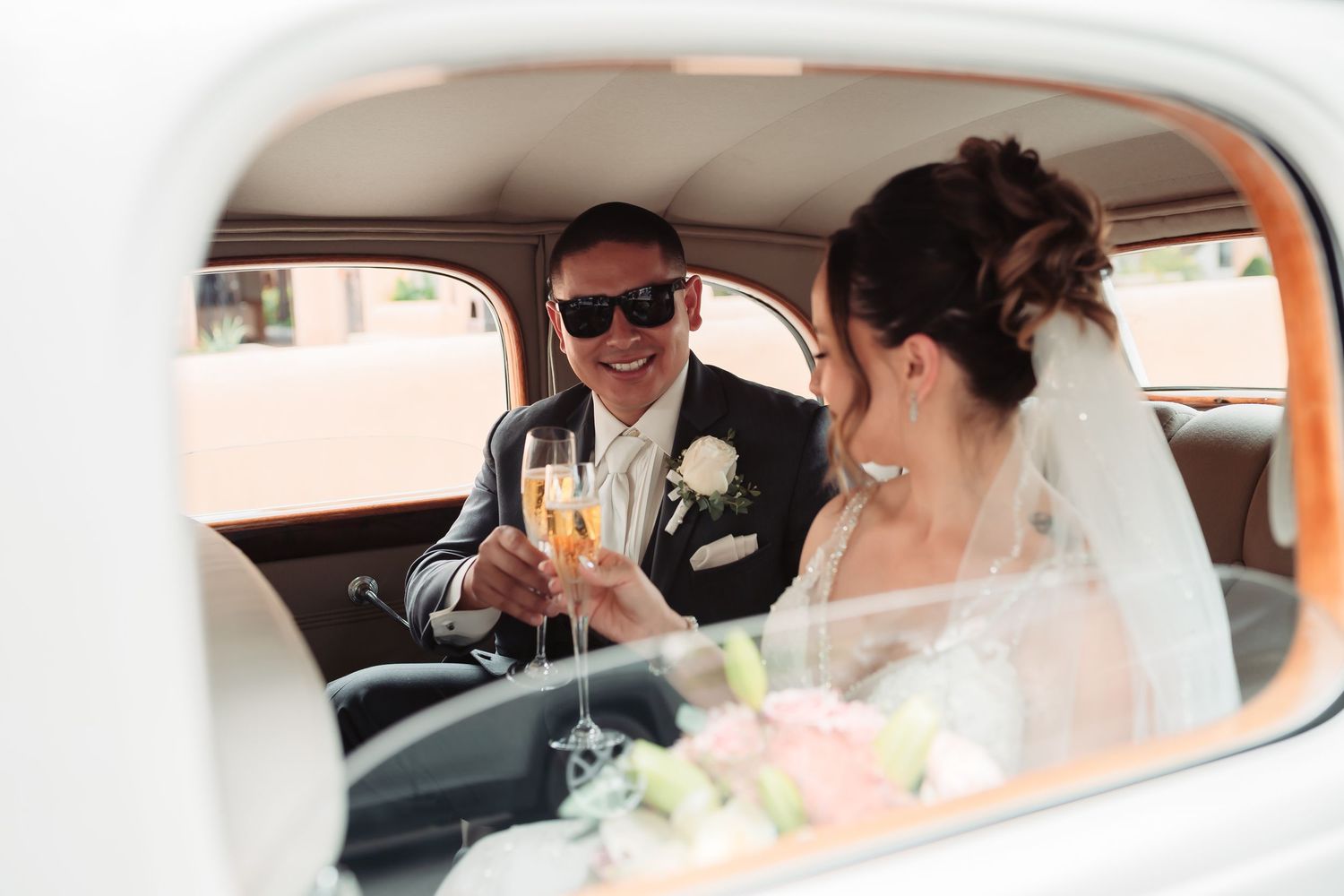 Wedding couple sits together in vintage white car with elegant interior and flowers.