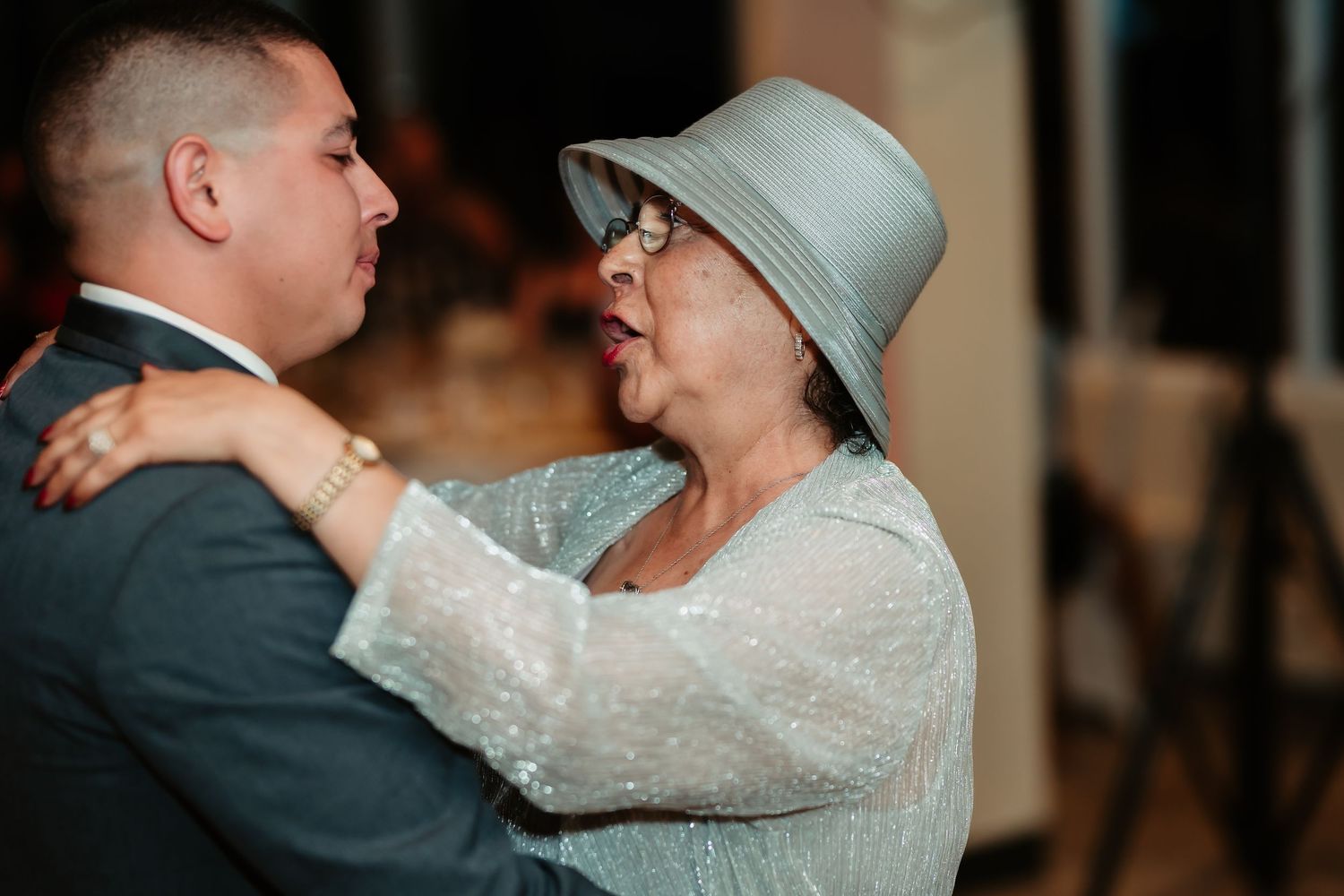 Couple embraces during their first dance at wedding reception with soft lighting and elegant decor.