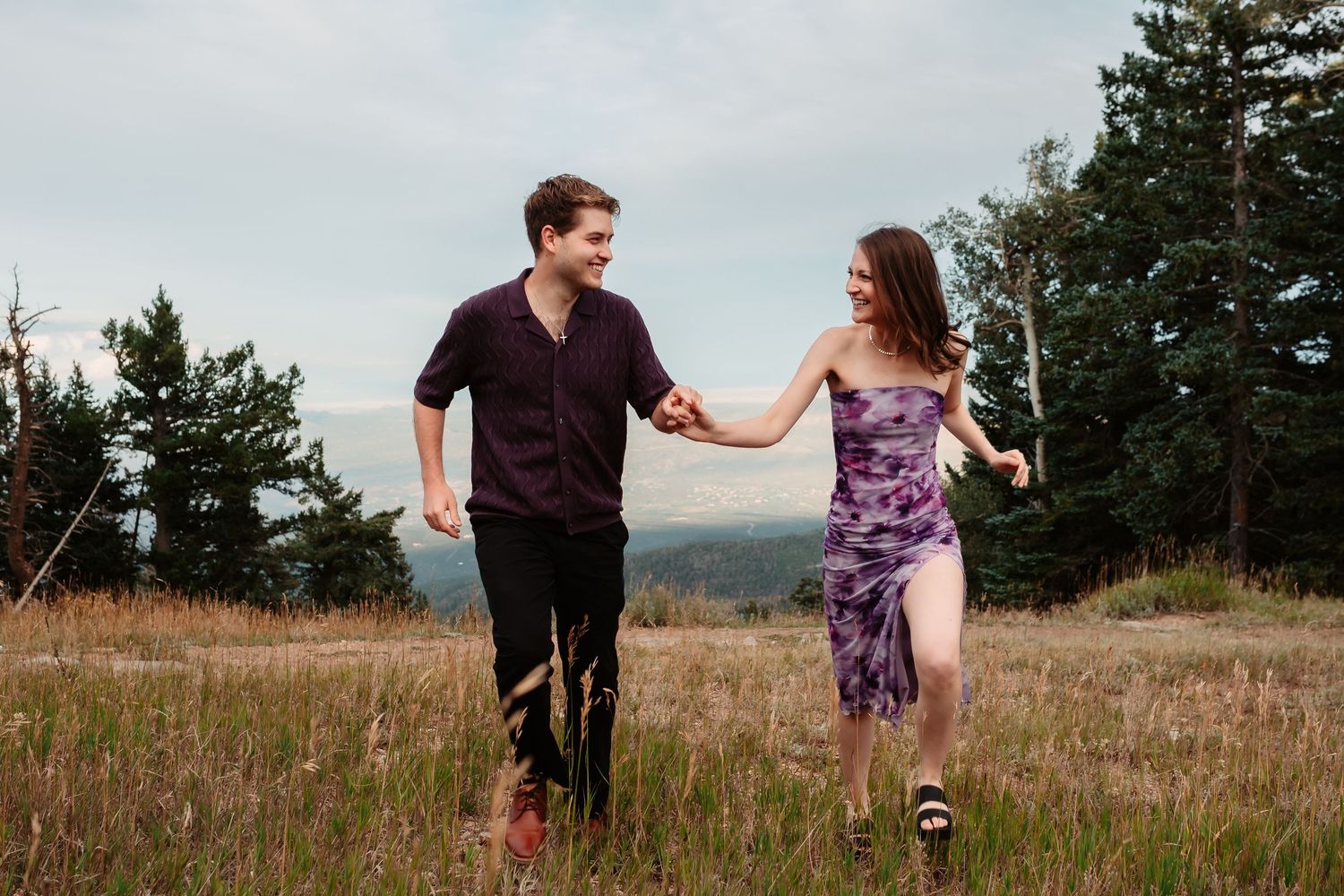 Two people walking hand in hand through a grassy mountain meadow.