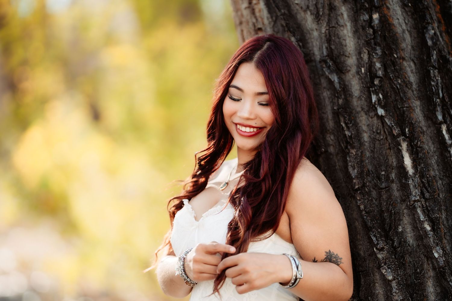 A woman in a white dress poses outdoors against a blurred autumn background with golden bokeh lighting.