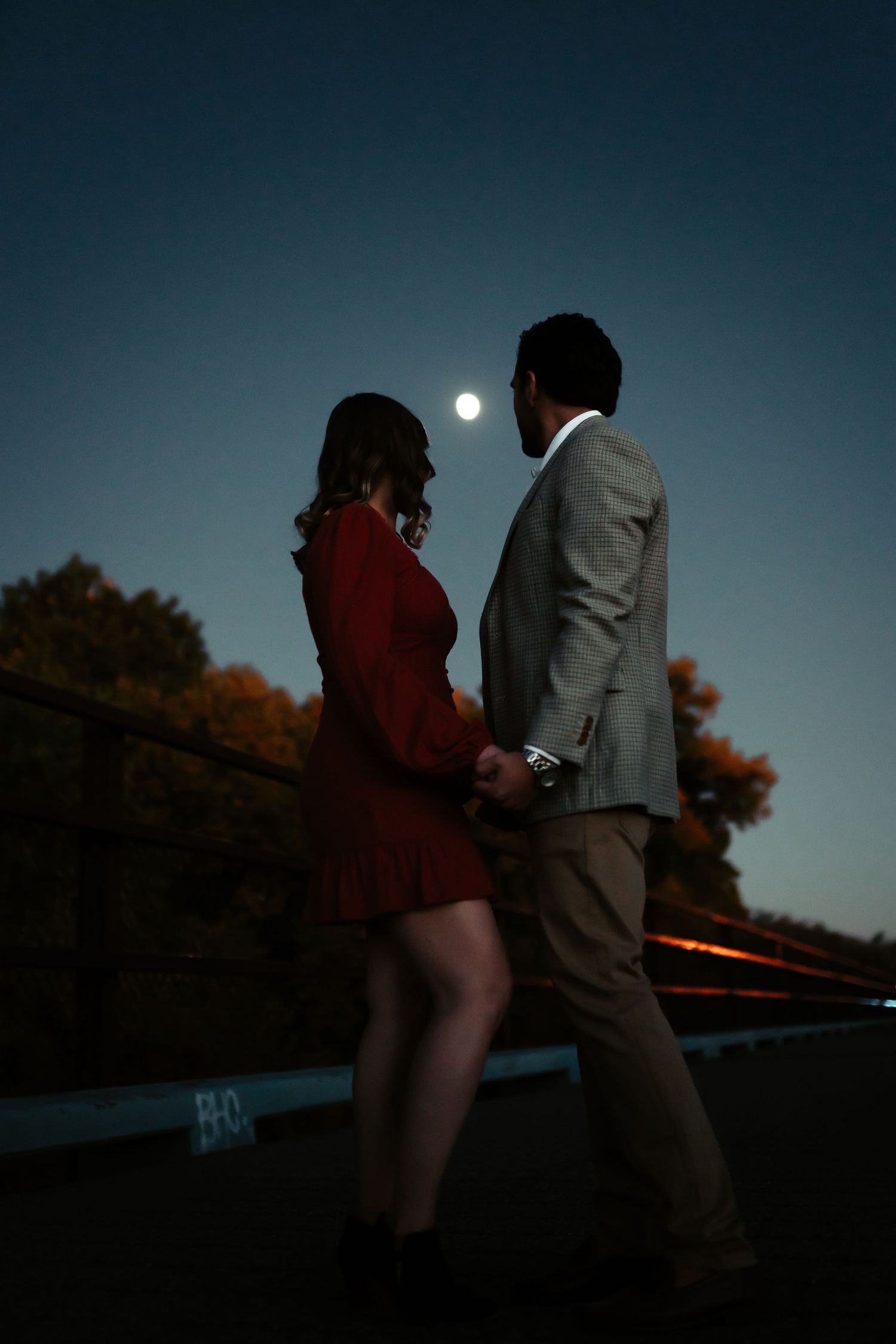 A couple in formal attire walks together at dusk against a moody blue sky backdrop.
