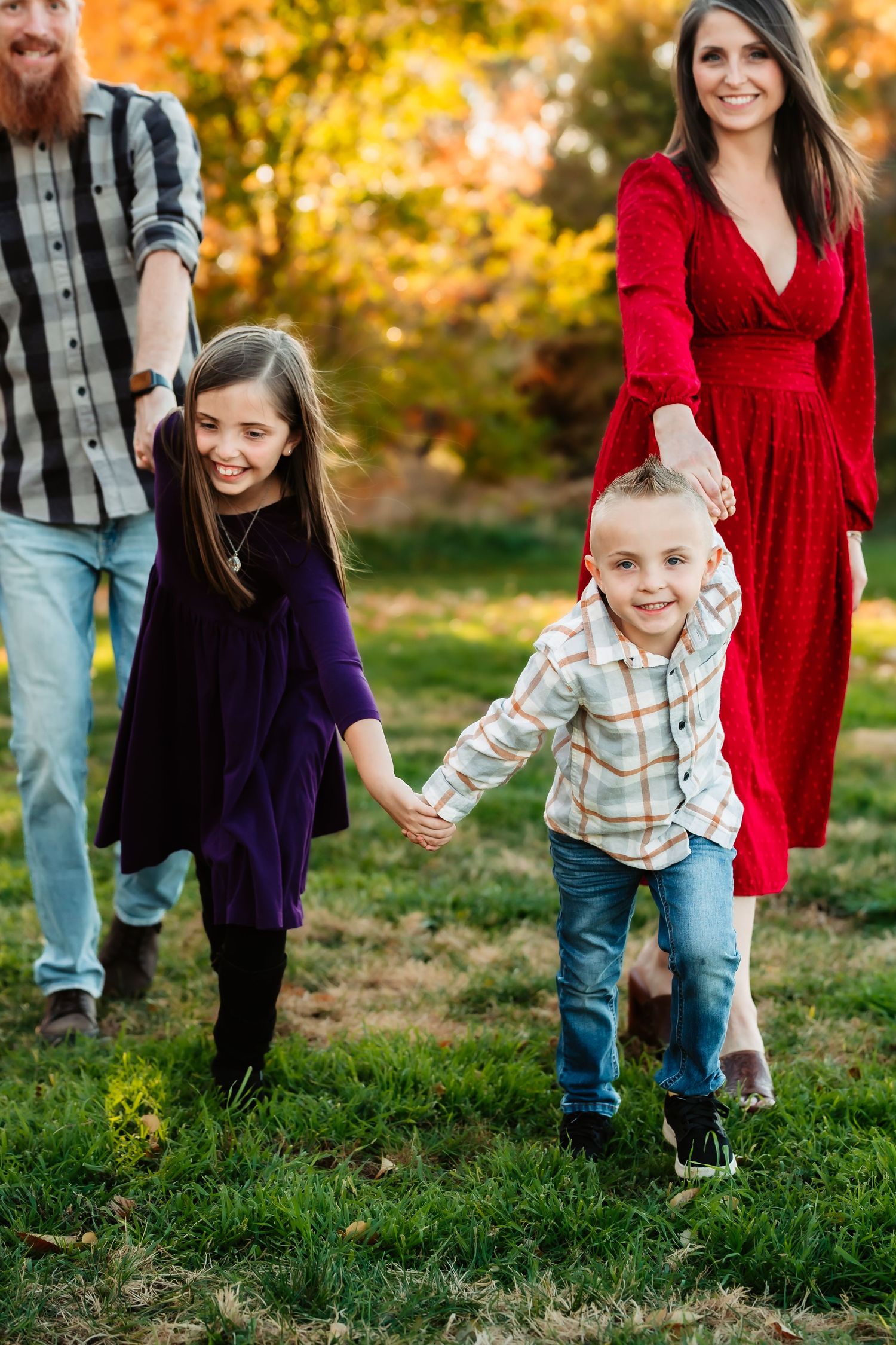A family plays together in a grassy field during golden hour with vibrant autumn colors in the background.