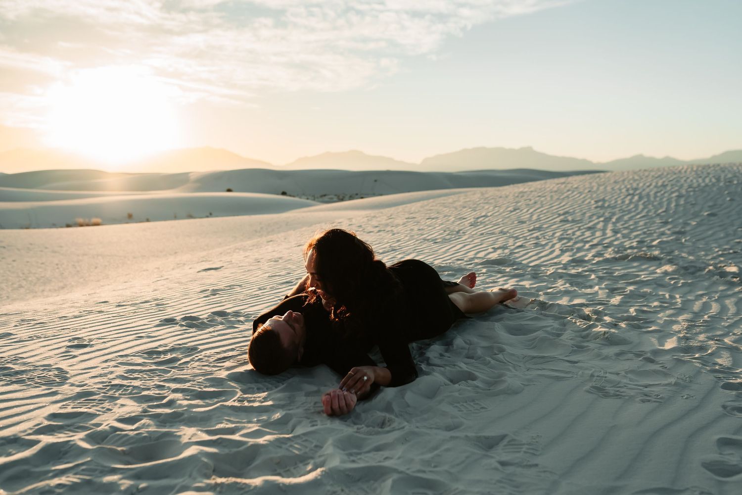 A figure lying on pristine white sand dunes at sunset with dramatic shadows and golden light.