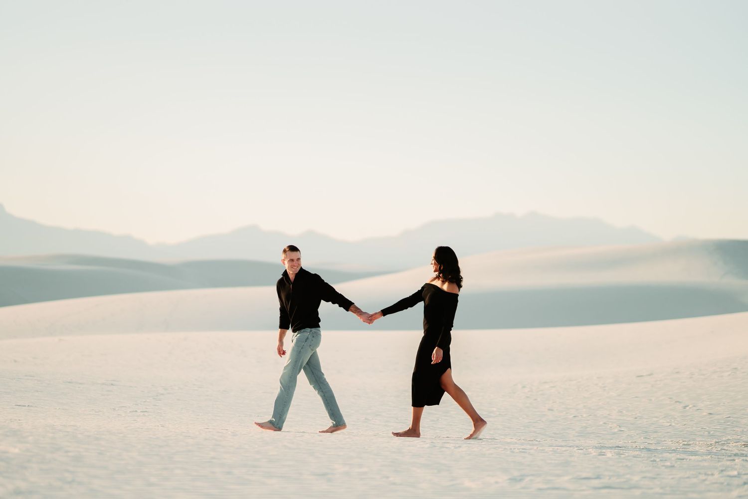 A couple holds hands while walking across the pristine white sand dunes at White Sands National Park in New Mexico.