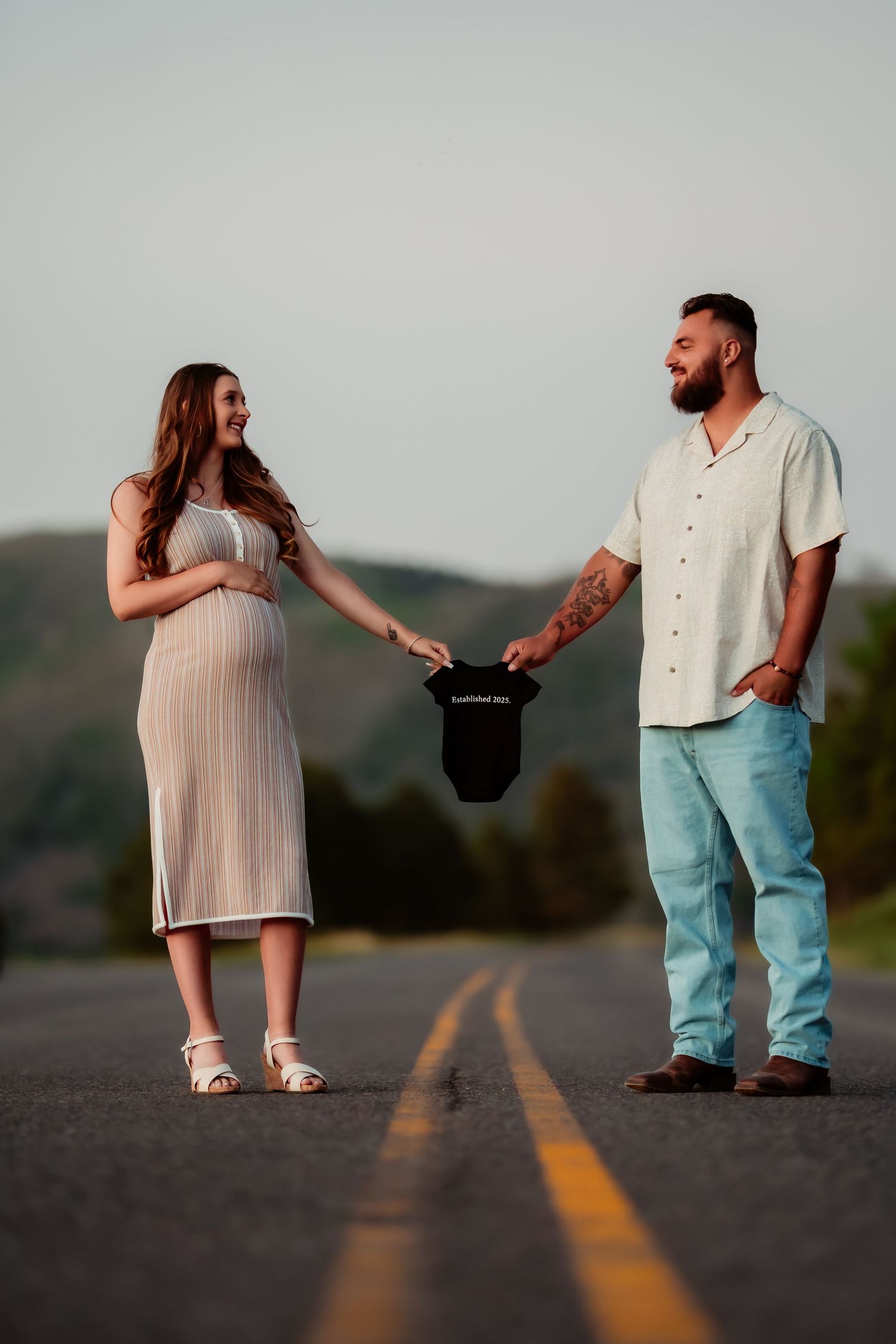 A couple stands together on a road at sunset, creating a series of romantic poses against a mountain backdrop.