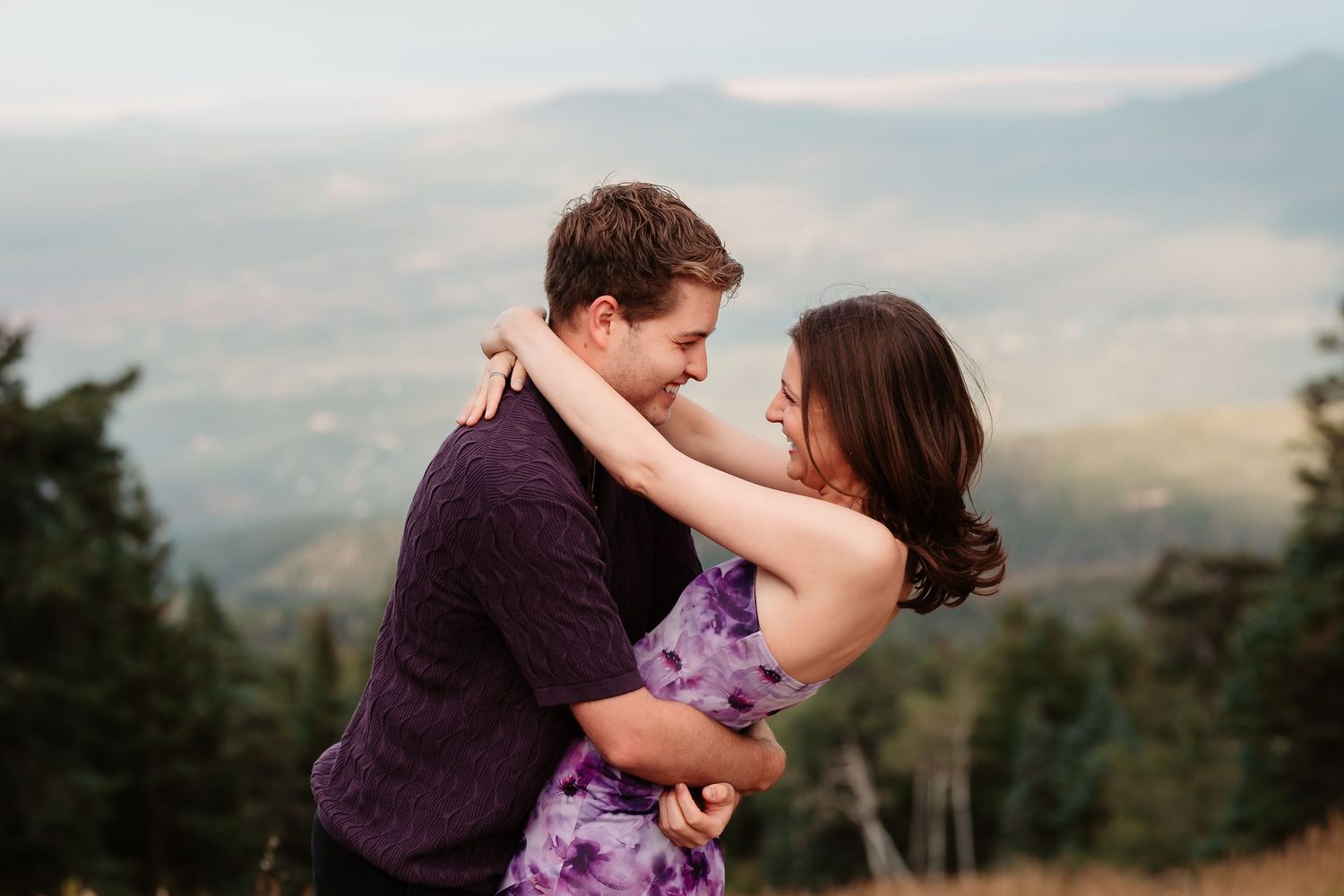 Romantic dance pose on mountain overlook with dramatic valley views and sunset sky in background.