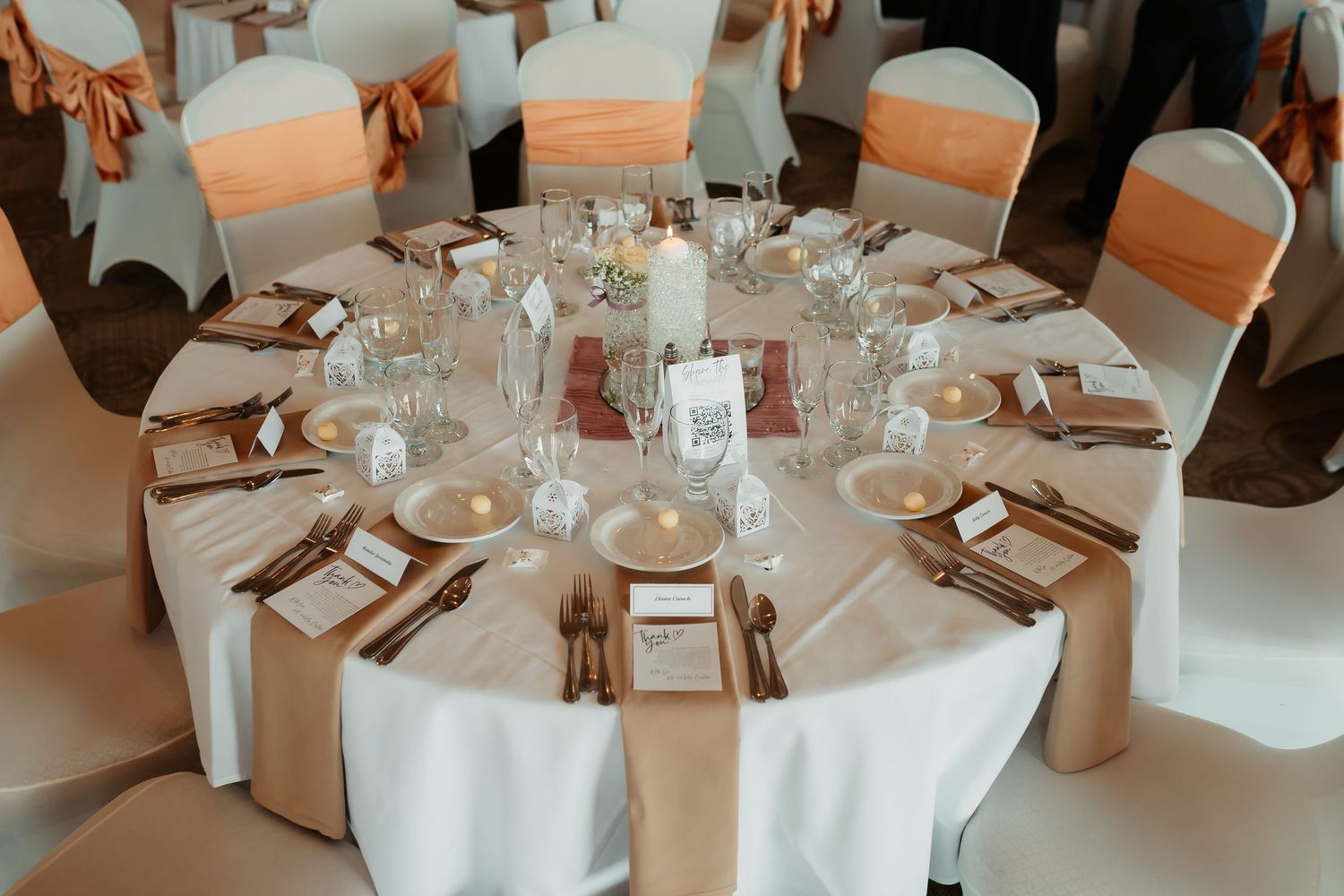 Wedding reception table settings with white linens, floral centerpieces, and soft peach lighting create an elegant atmosphere.