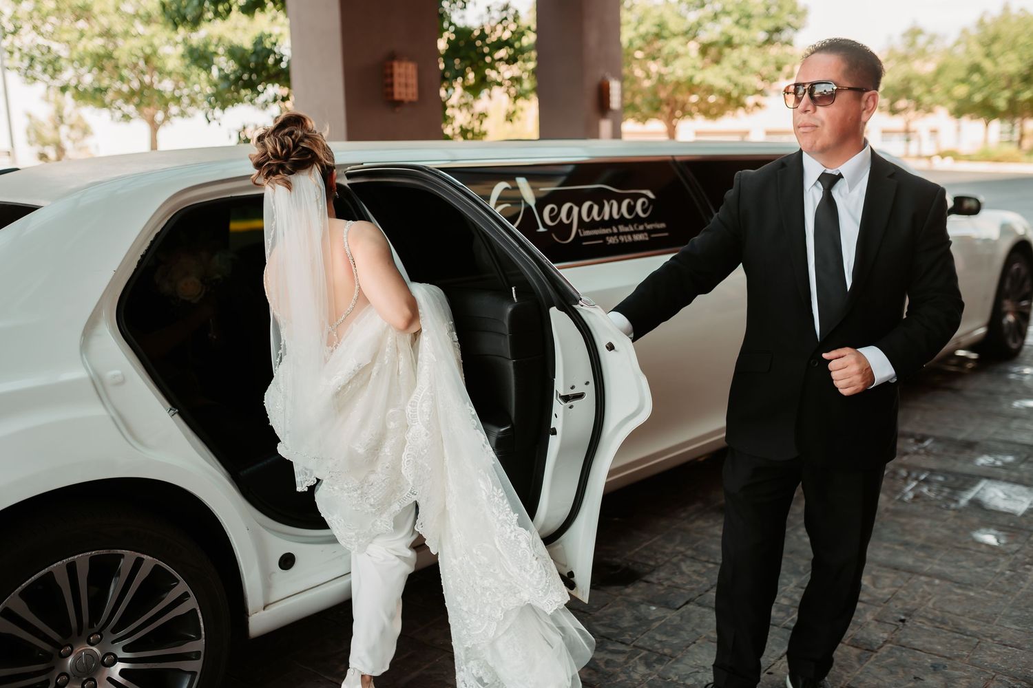 The groom leads his bride to a parked white limousine after their wedding ceremony.