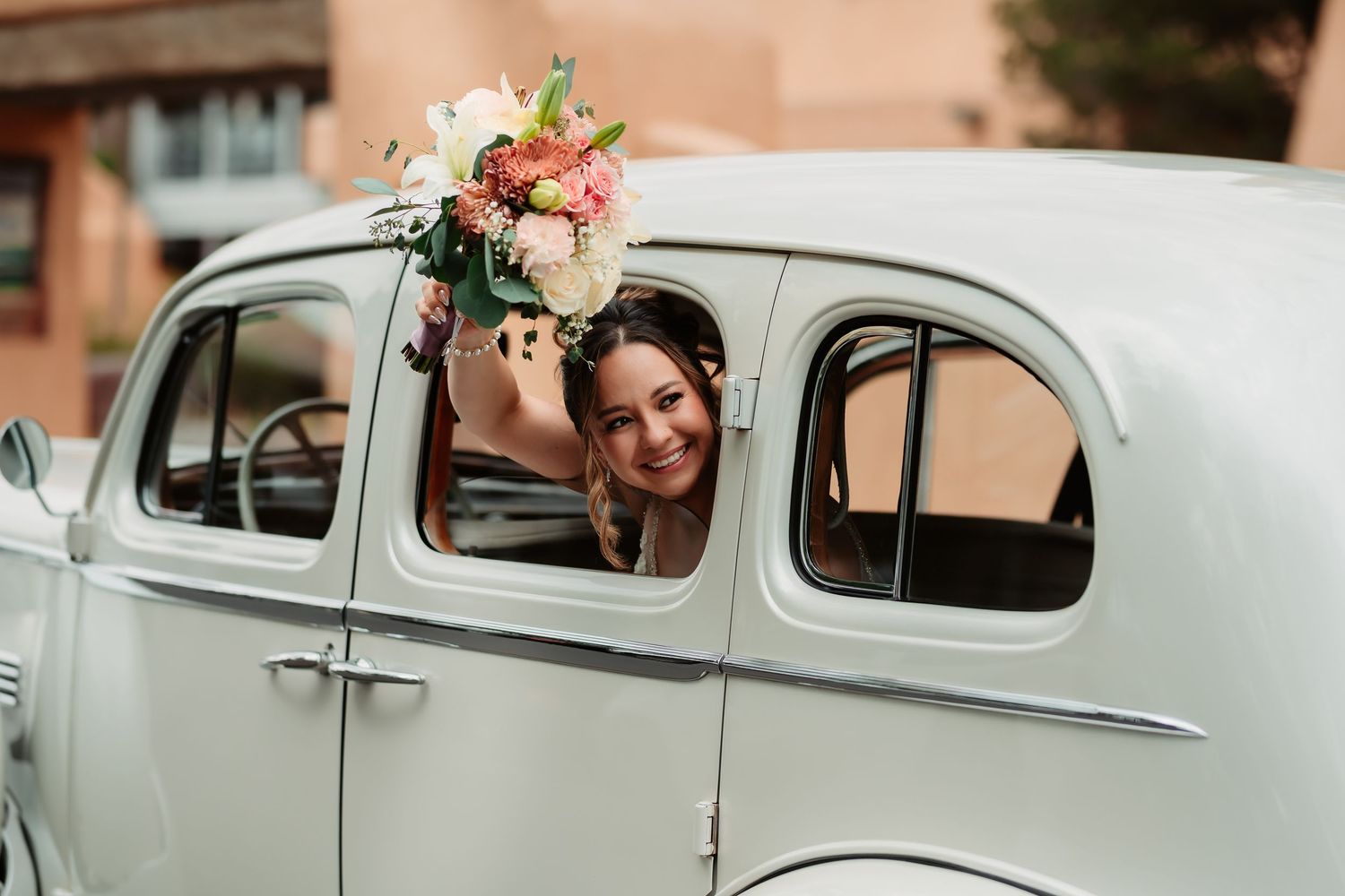 A vintage white classic car decorated with floral arrangements and 'just married' signage for a wedding celebration.