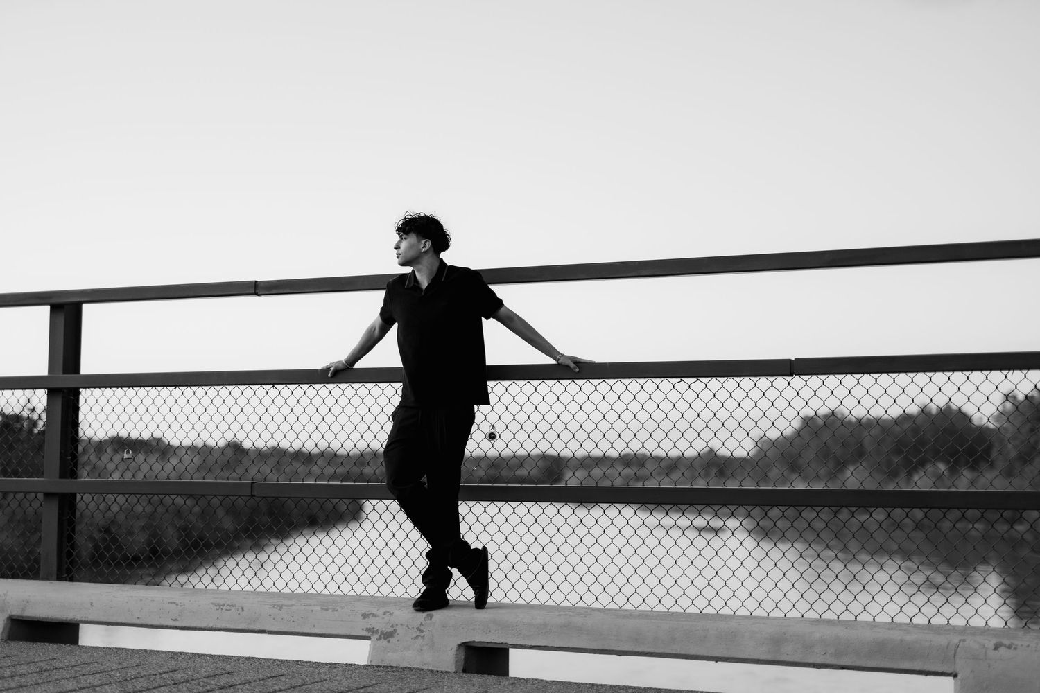 Silhouette of person leaning on bridge railing at sunset.
