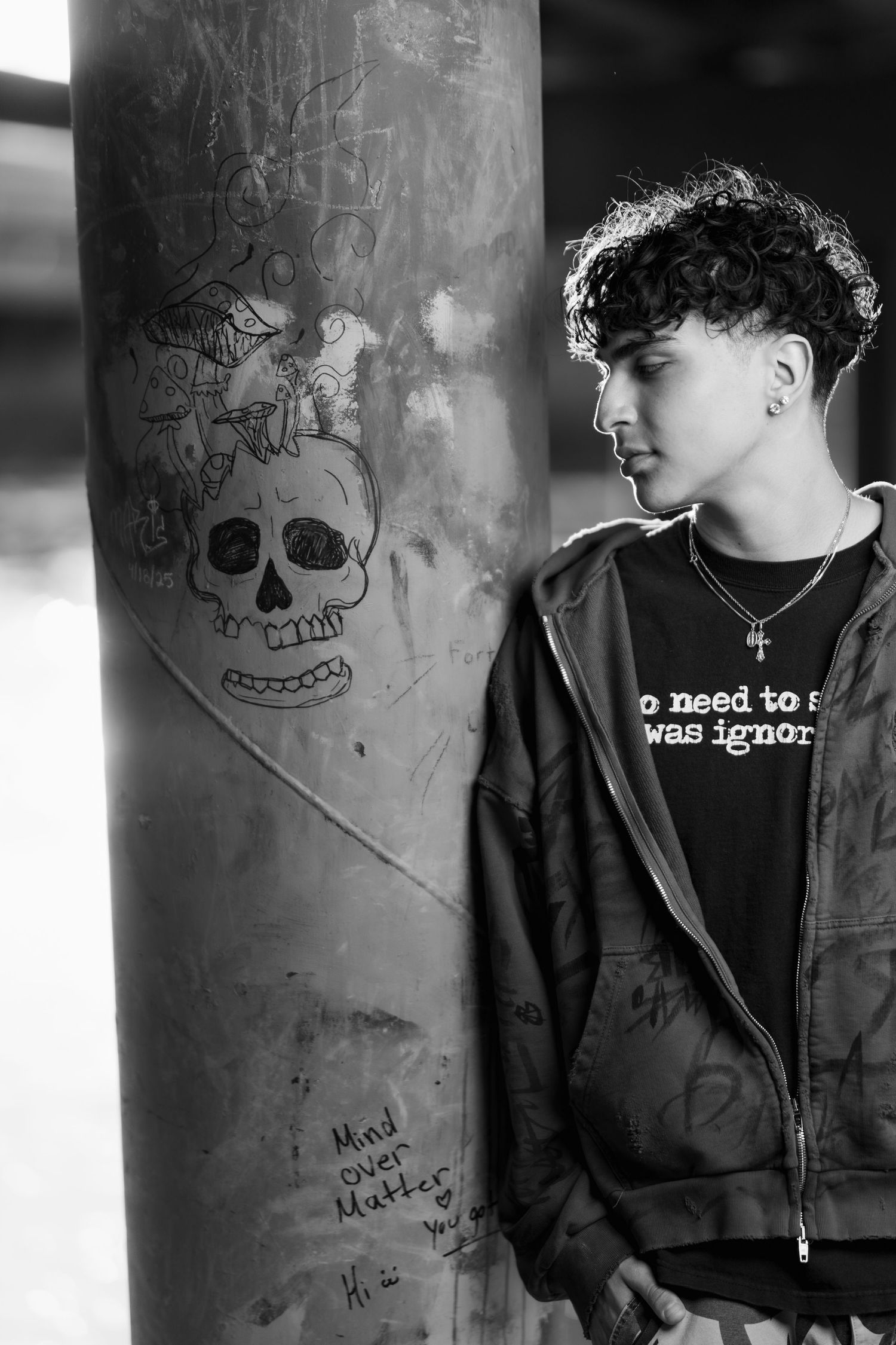 Black and white photo showing graffiti of a skull on a wall next to someone in a dark hoodie.
