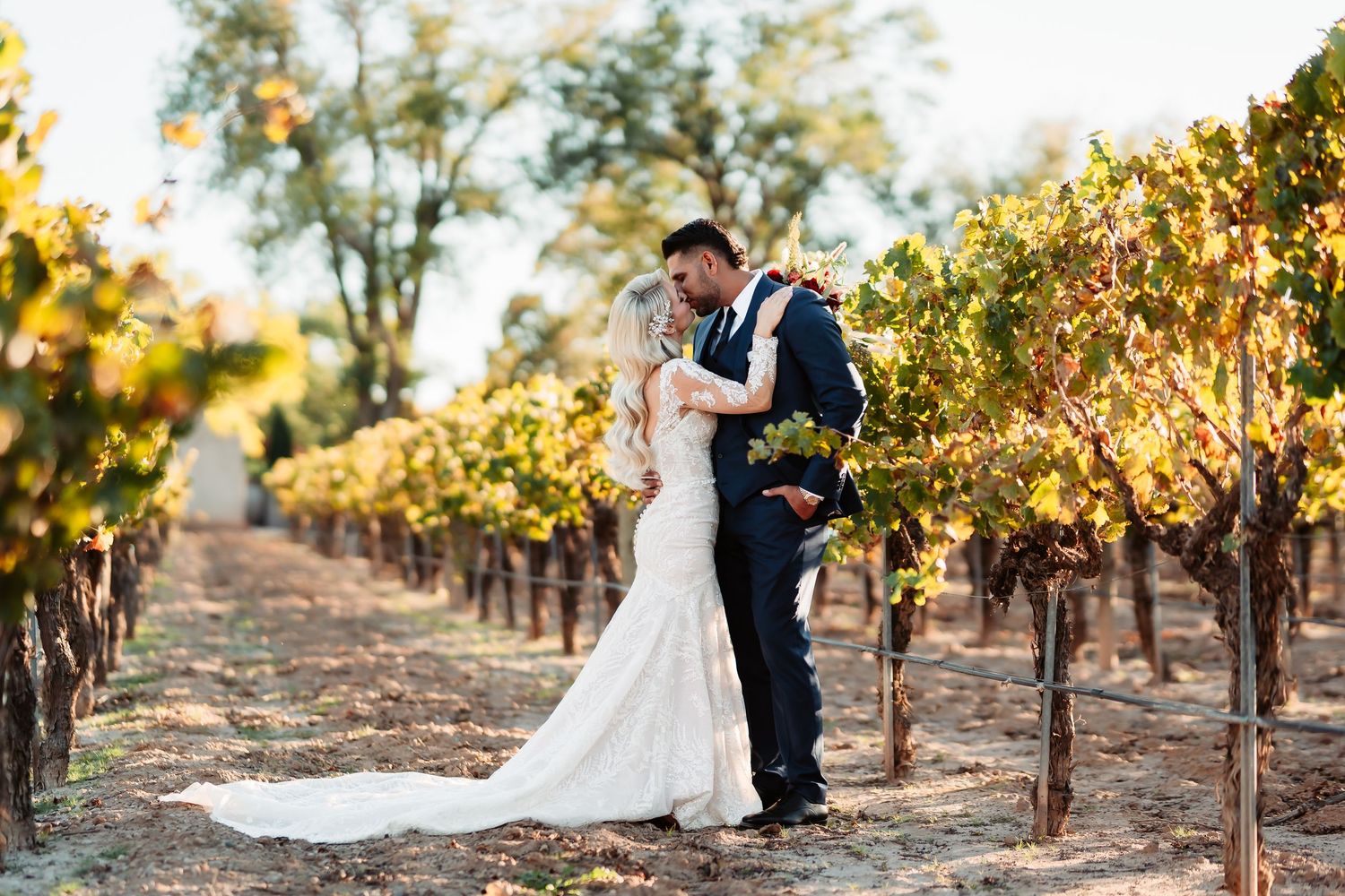 A couple shares a romantic moment among golden autumn vineyard rows at sunset.