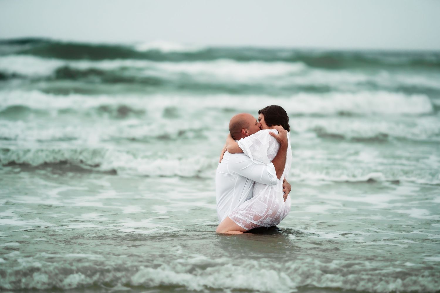 A person in white clothing lies gracefully in shallow ocean waves creating an artistic beach portrait.