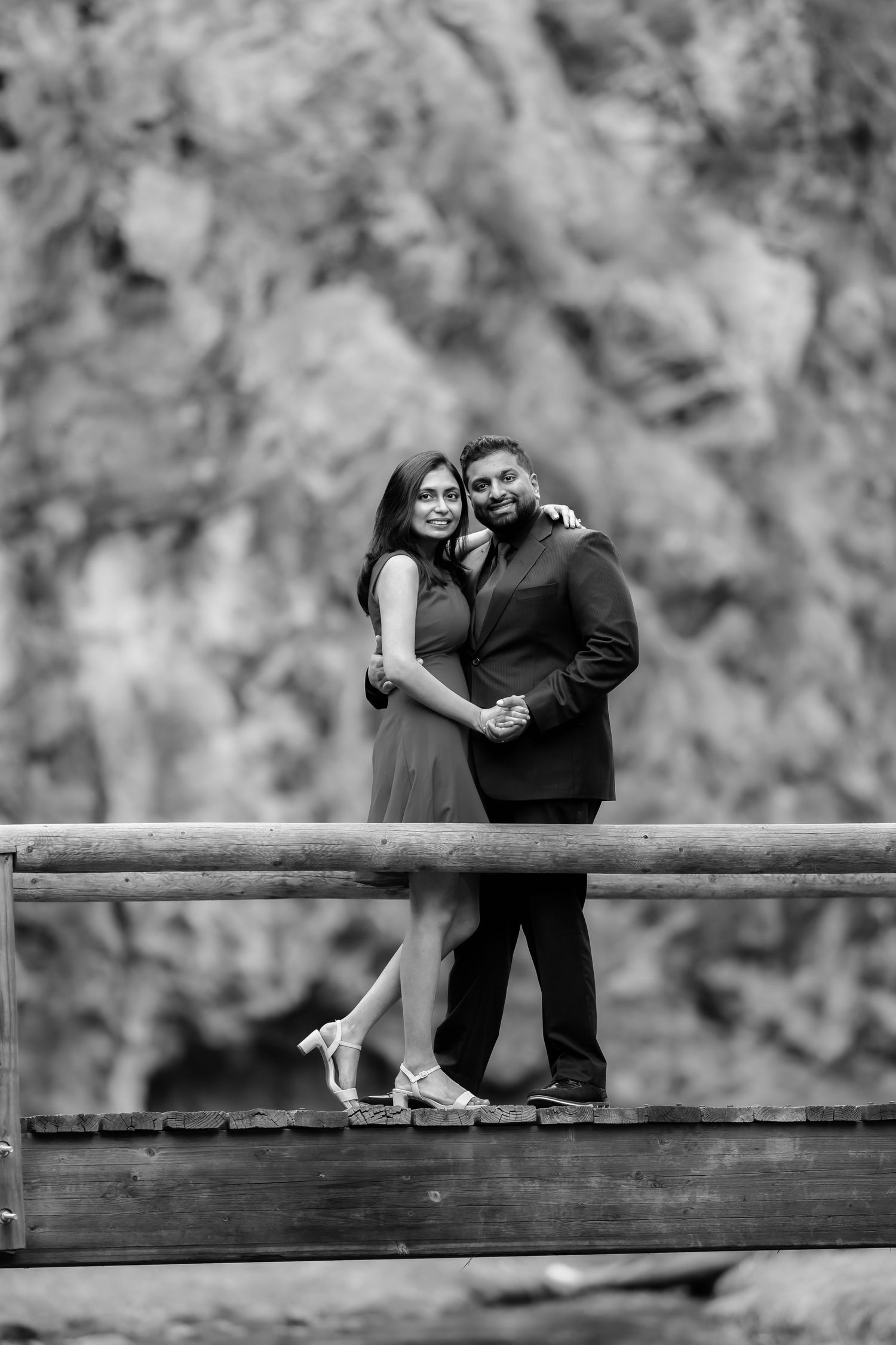A couple poses together on a wooden bridge in black and white formal attire.