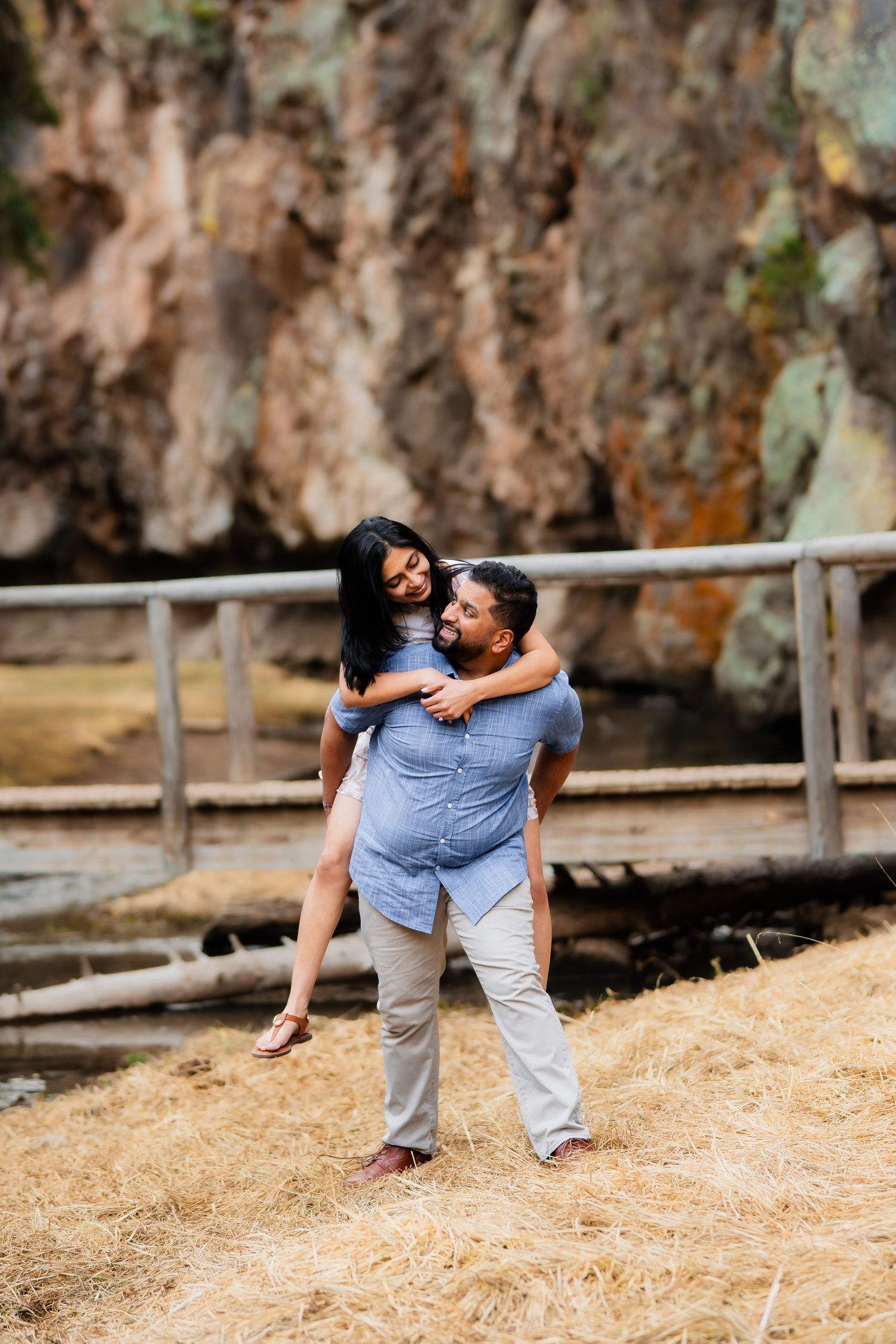 A playful piggyback pose against a dramatic rocky landscape background.