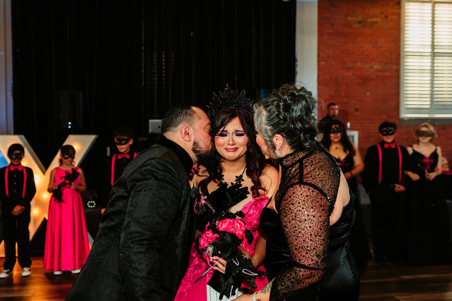 A festive celebration scene with a bright pink dress surrounded by guests in formal black attire.