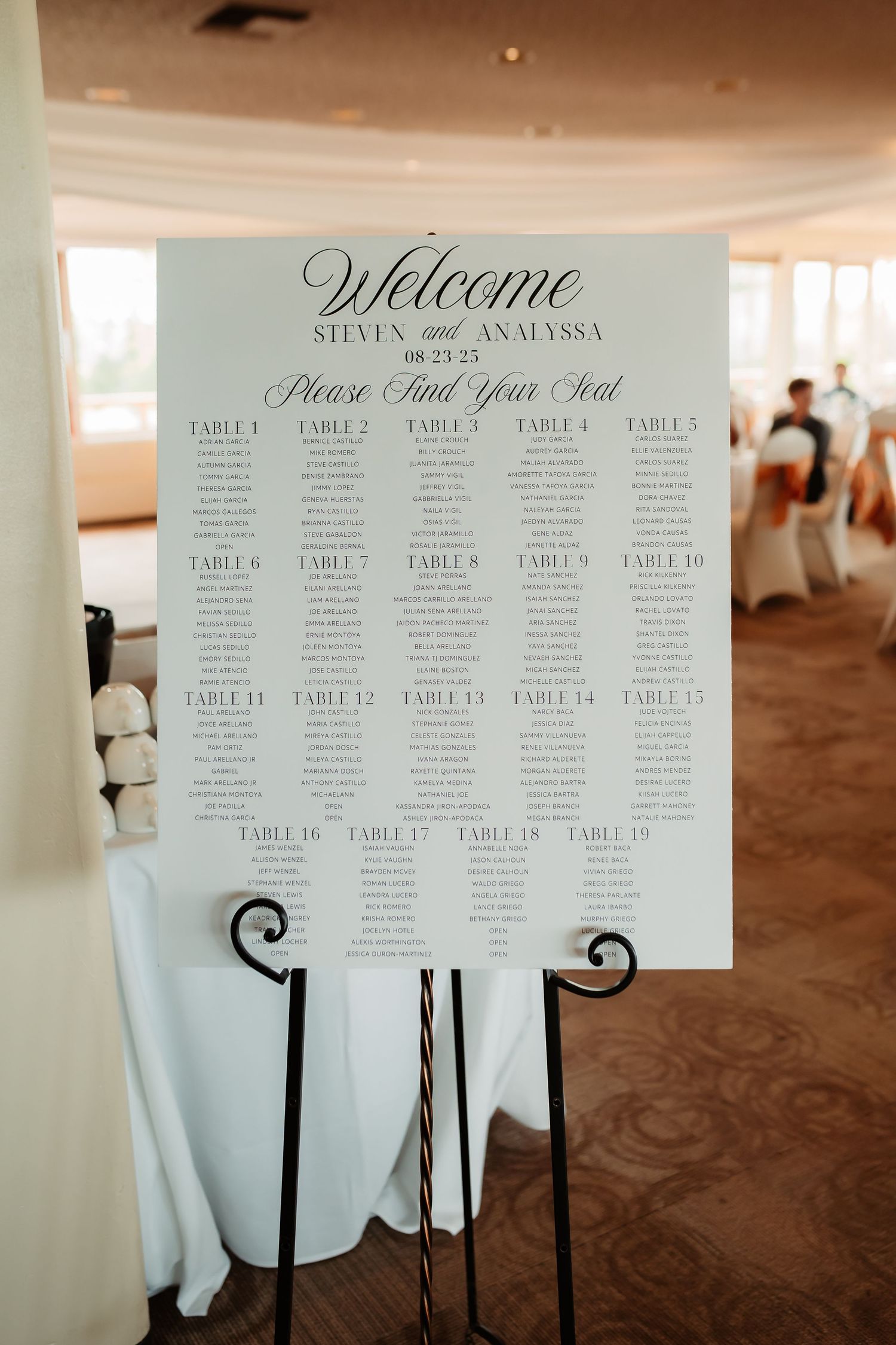 Wedding reception seating chart displayed on elegant white signs with ornate black stands at venue entrance.
