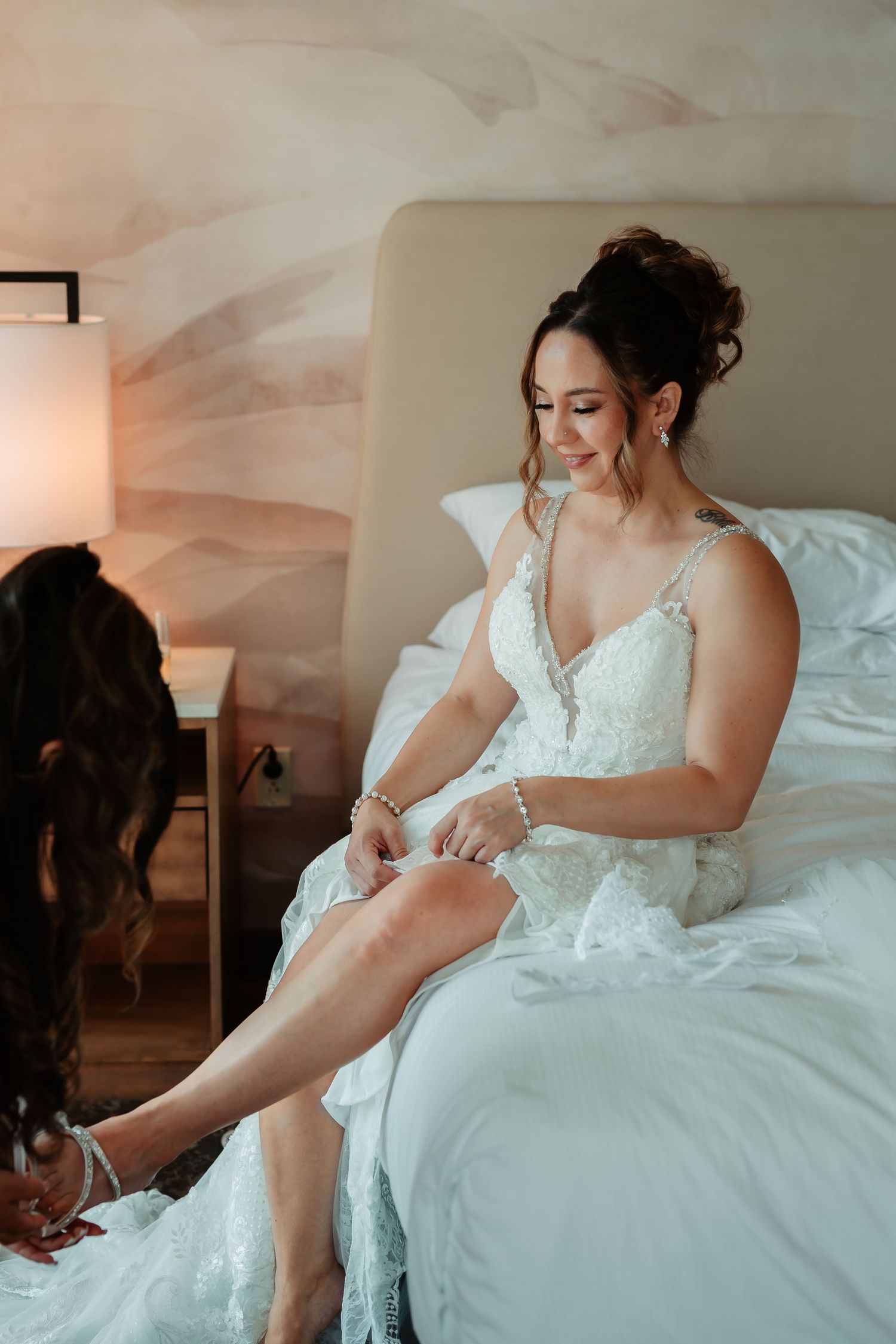 A wedding dress detail shot showing someone fastening delicate pearl buttons on a white lace gown.