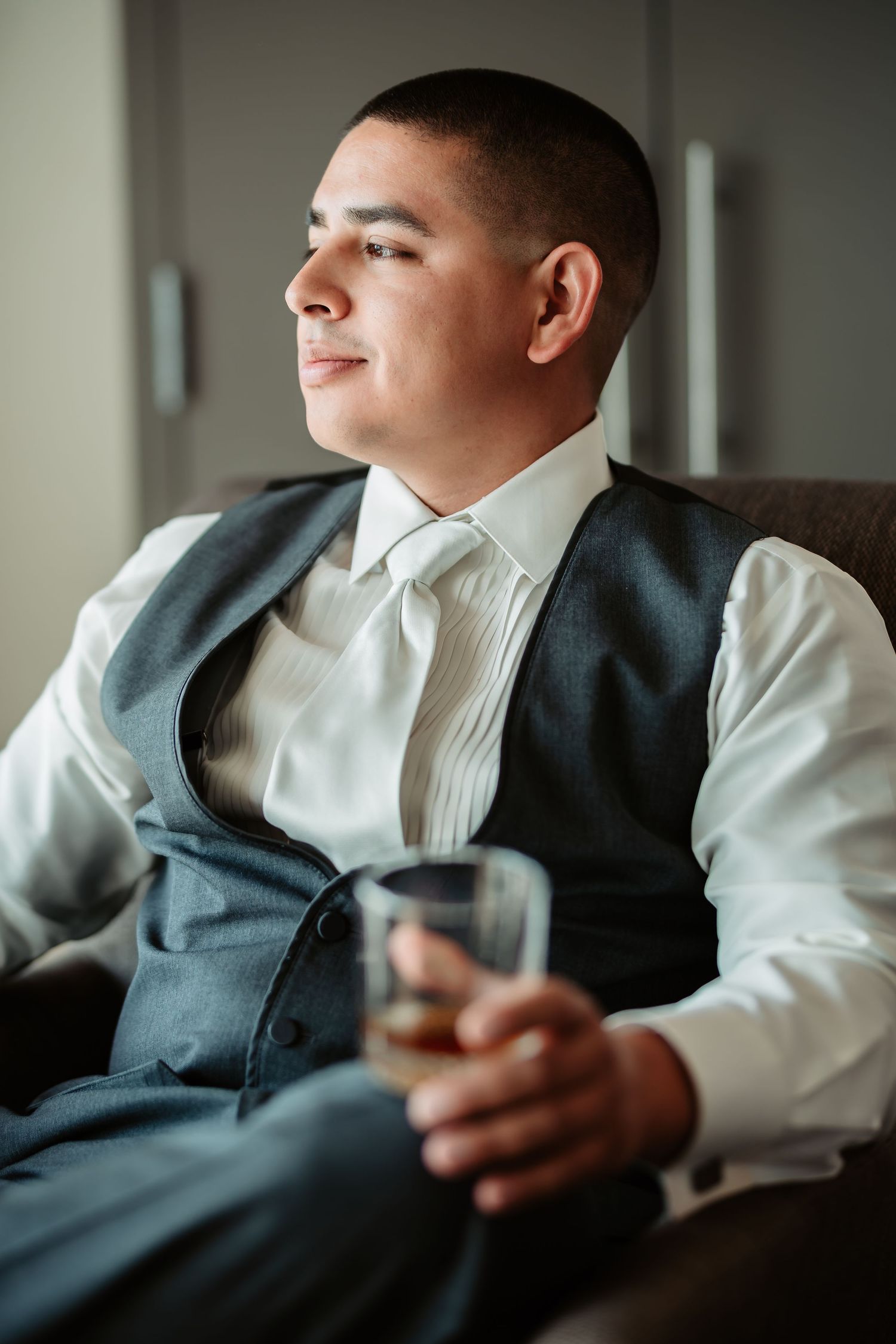 Wedding day preparation moments captured in moody lighting while seated in modern gray armchair.