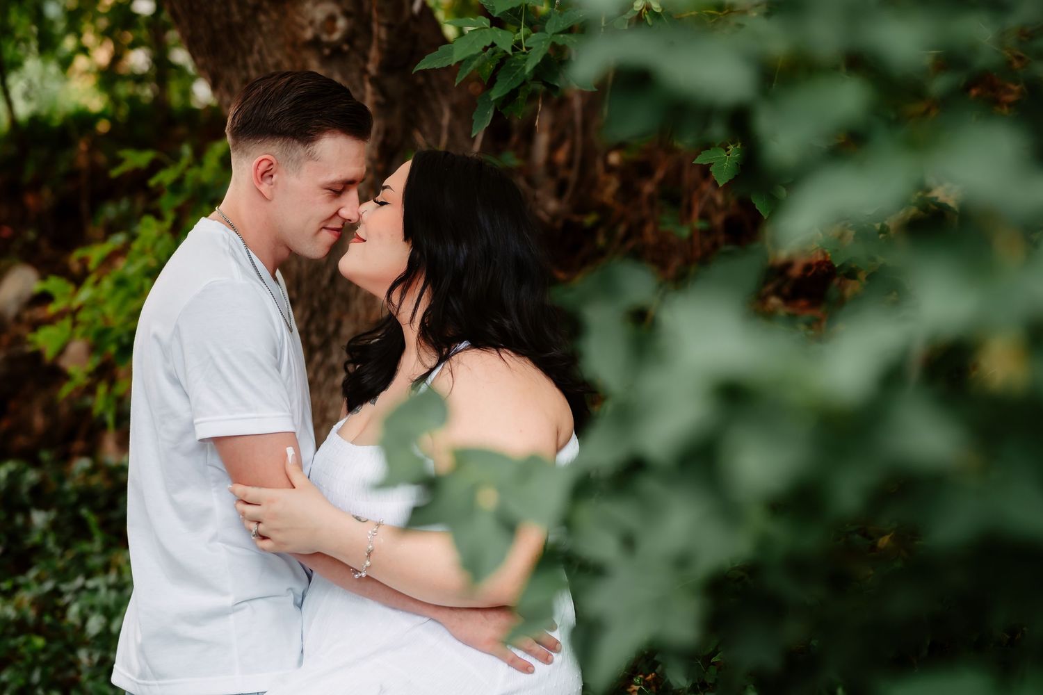 Romantic couple shares intimate moments in garden setting surrounded by lush green foliage.