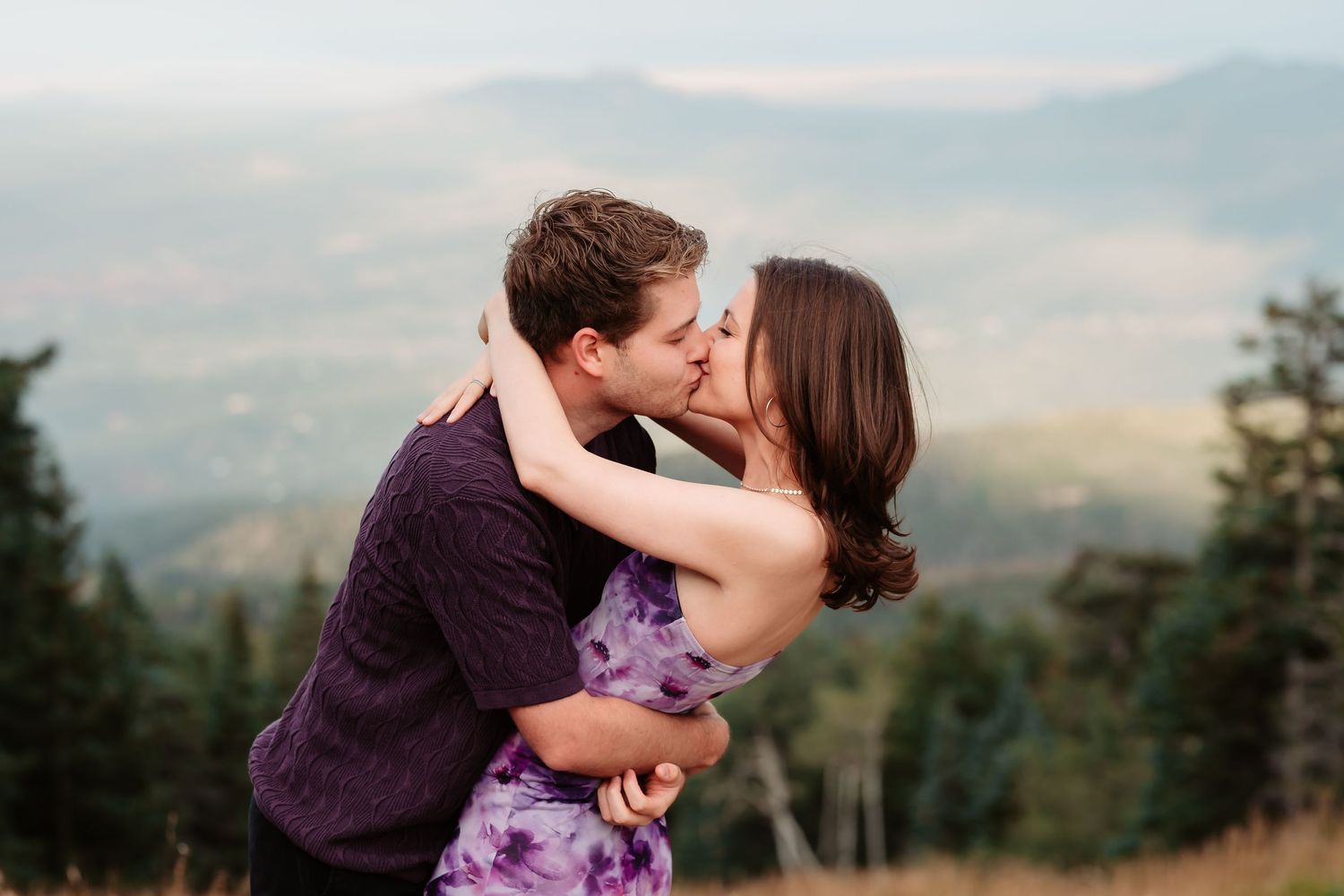 Romantic kiss captured during mountain engagement photoshoot at golden hour.